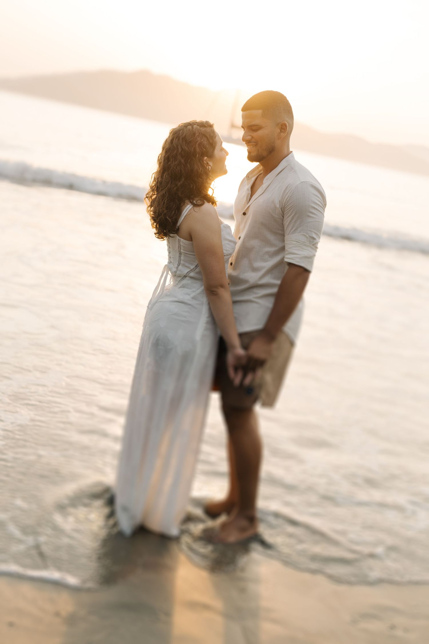 Romantic sunset beach portrait of couple standing in shallow ocean waters.