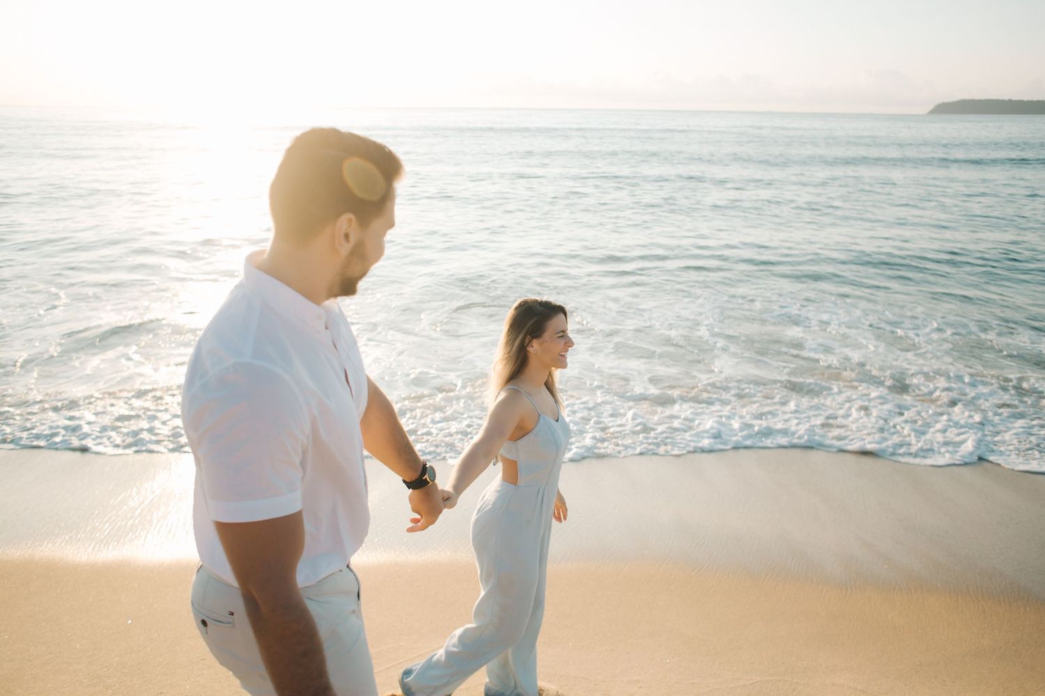 Two people in white clothing enjoying a sunset beach walk together.