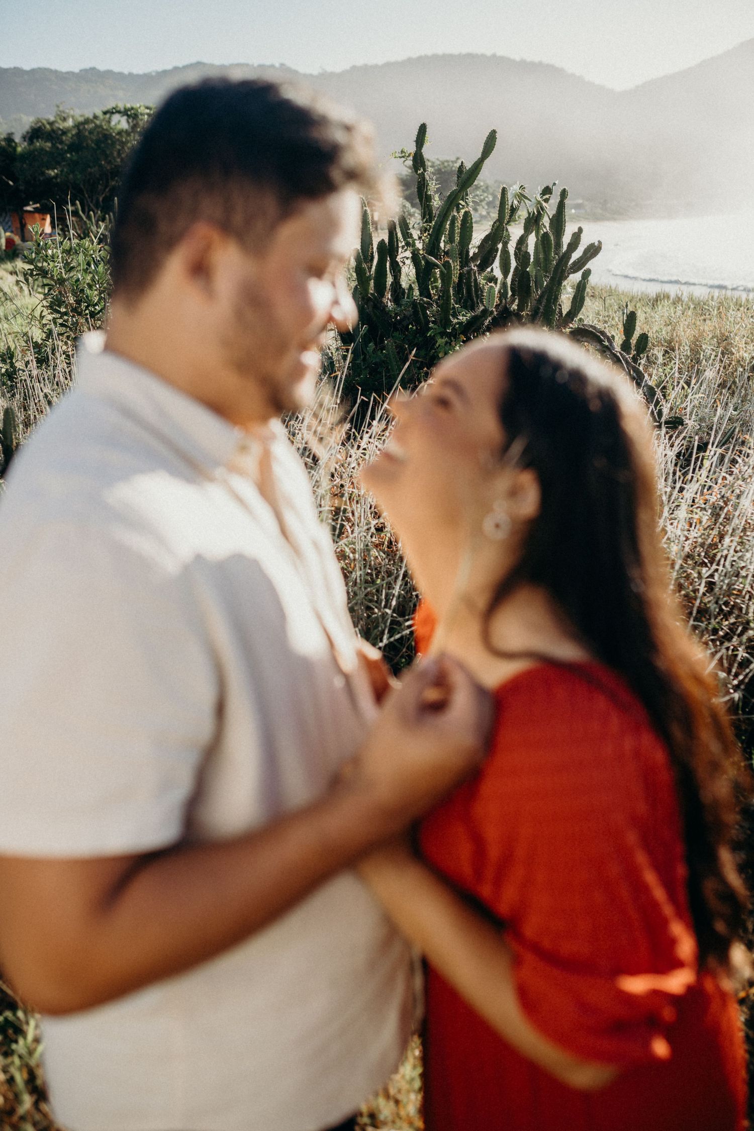 Romantic couple embraces on a hilltop with desert landscape and mountains in soft sunlight.