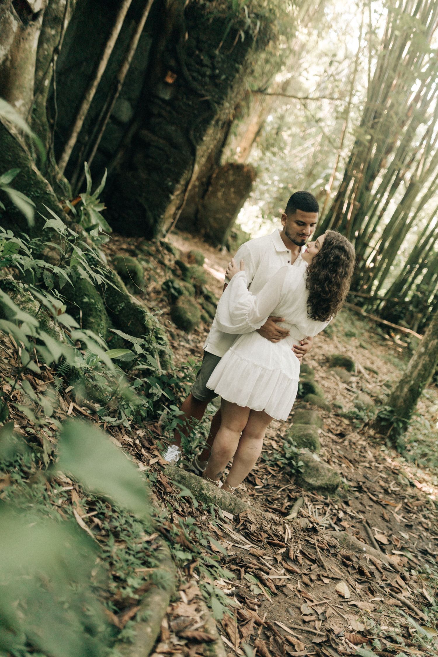 Forest photoshoot featuring couple in coordinated white outfits against lush green background.