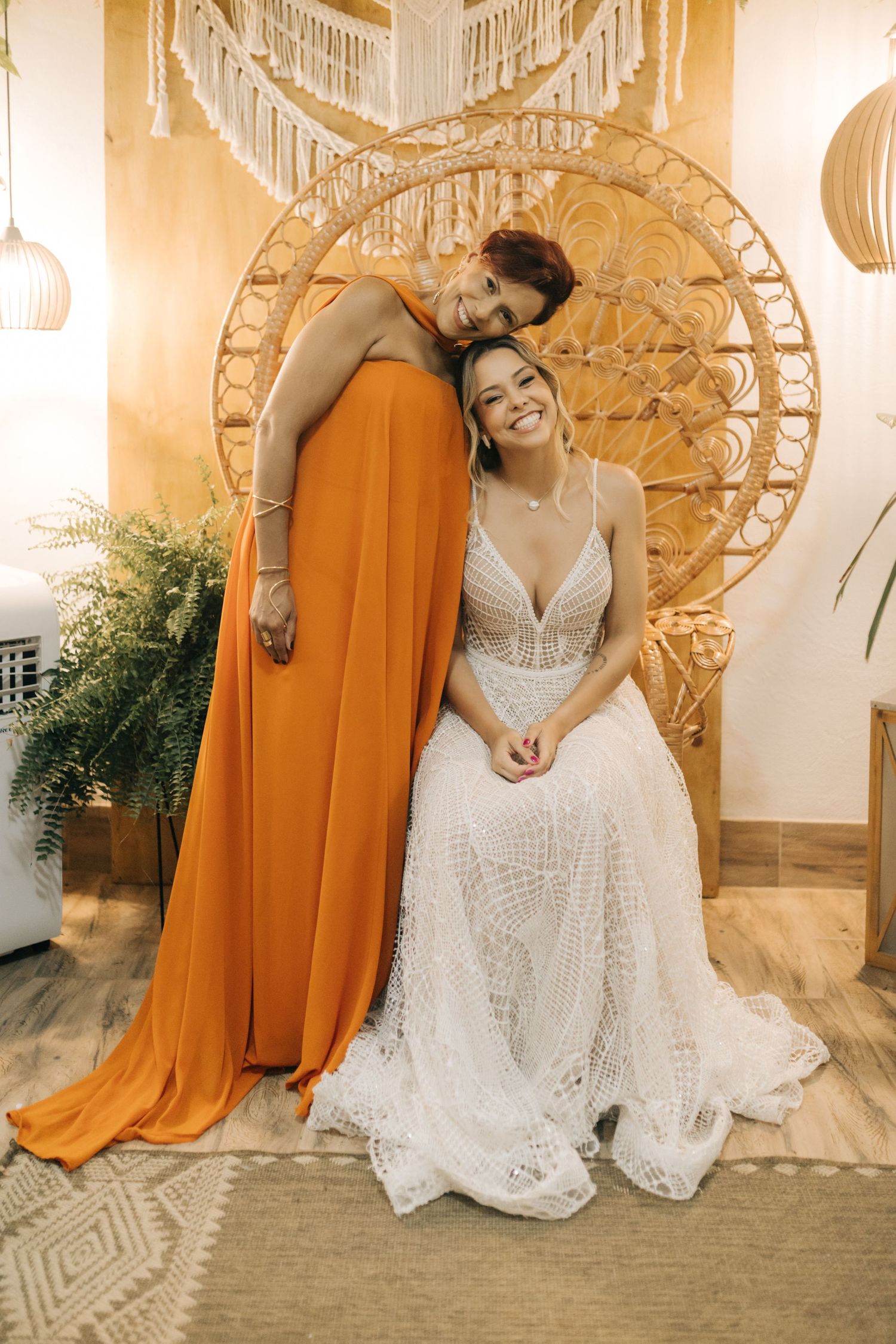 Joyful wedding portrait against woven peacock chair with orange and white dress contrast.