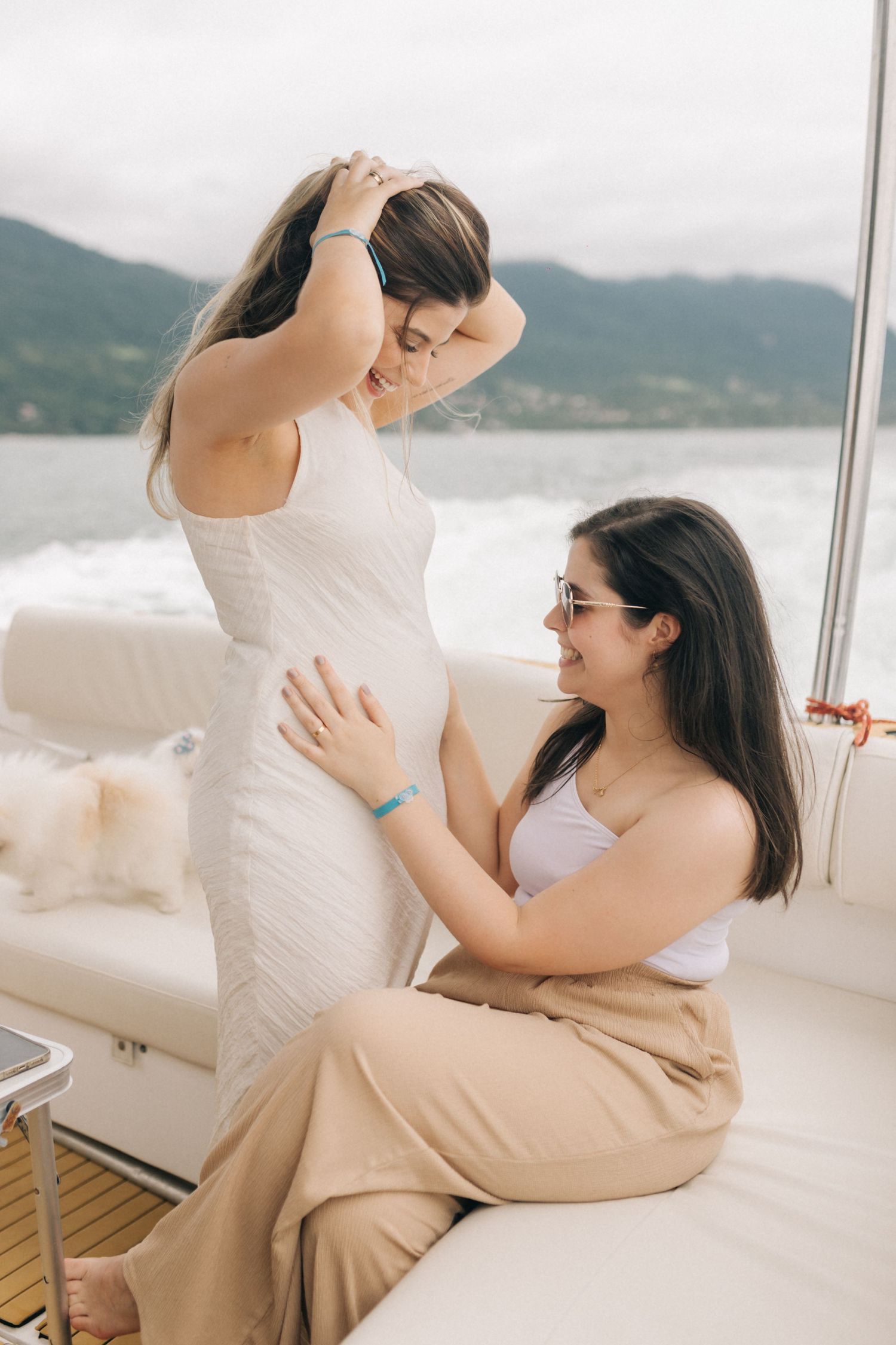 Two friends sharing laughter and embracing on a boat with mountains in background.