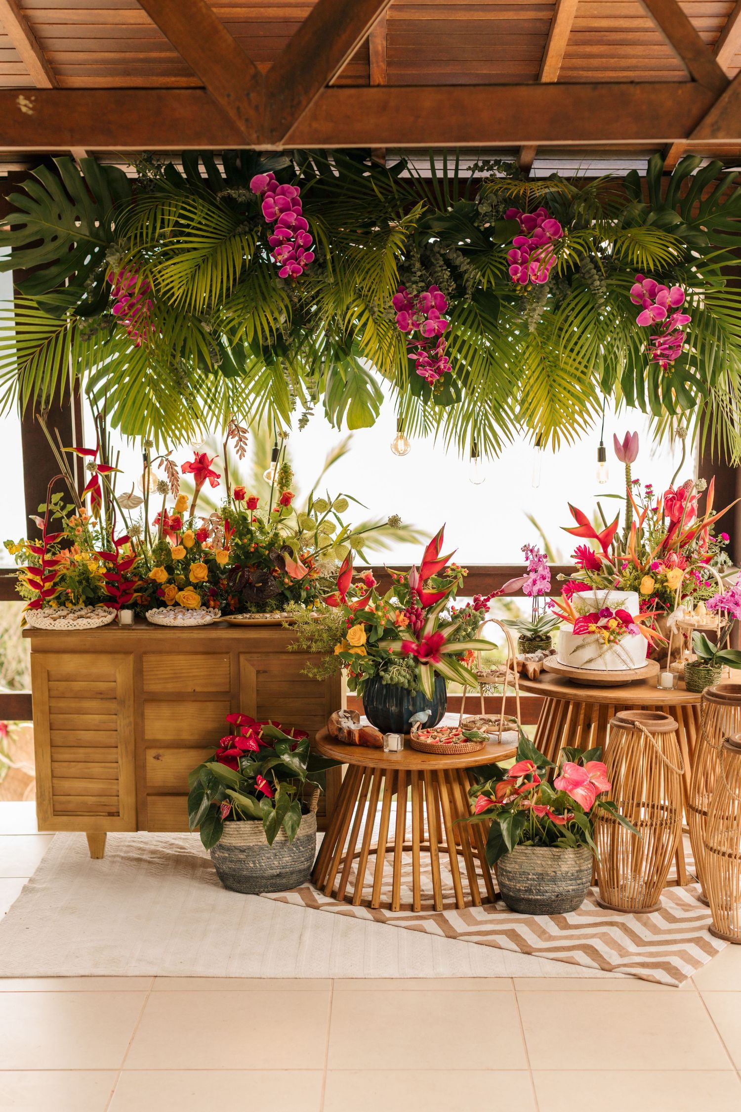 Tropical wedding decor featuring vibrant pink orchids, palm fronds, and rattan furniture arranged in an elegant outdoor setting.