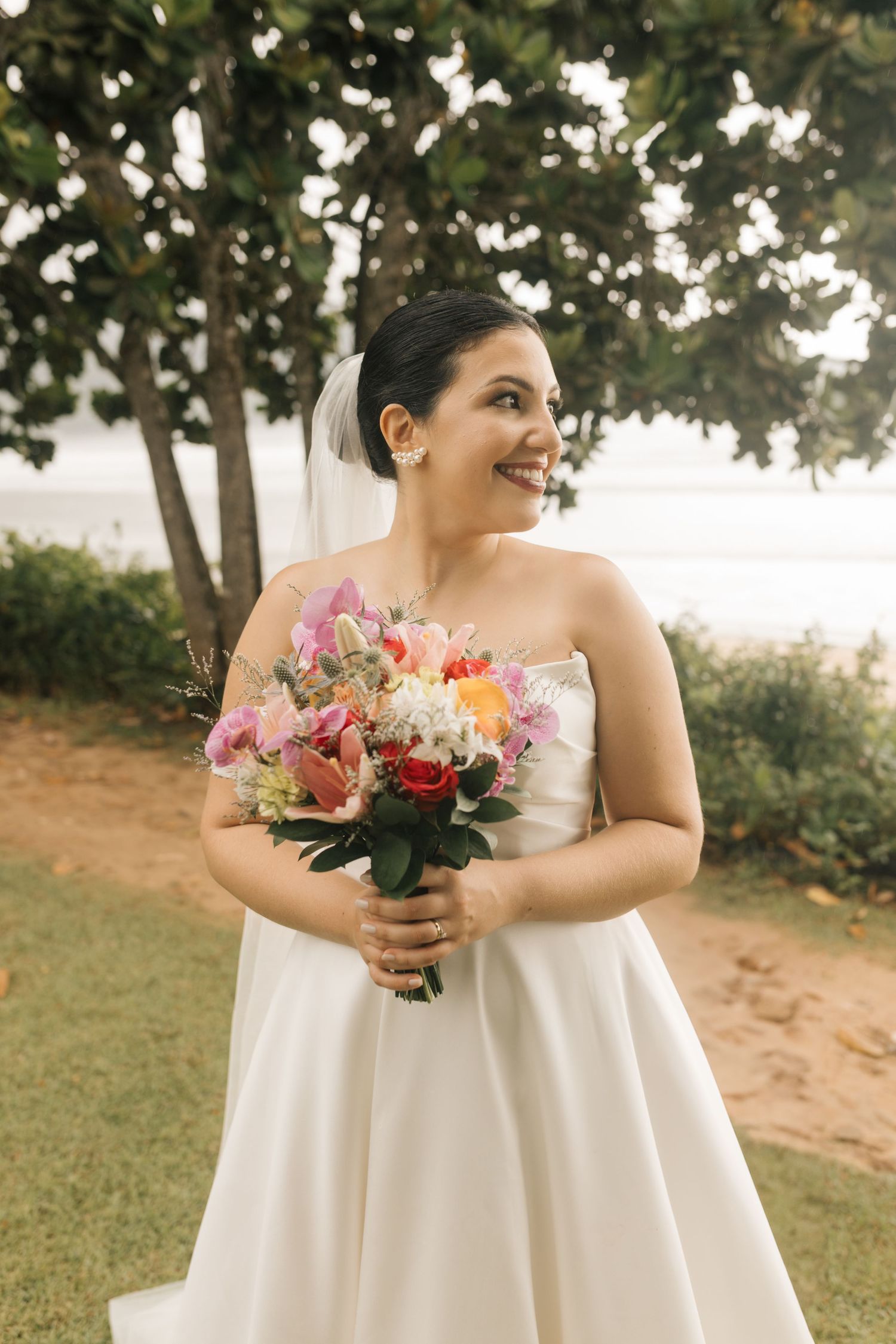 Bride in elegant white dress holding colorful floral bouquet outdoors.