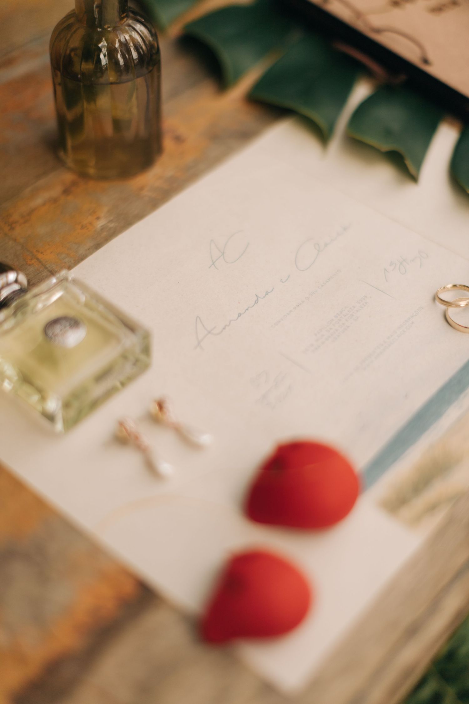 Handwritten wedding invitations with red heart accents and decorative bottles on a rustic wooden surface.