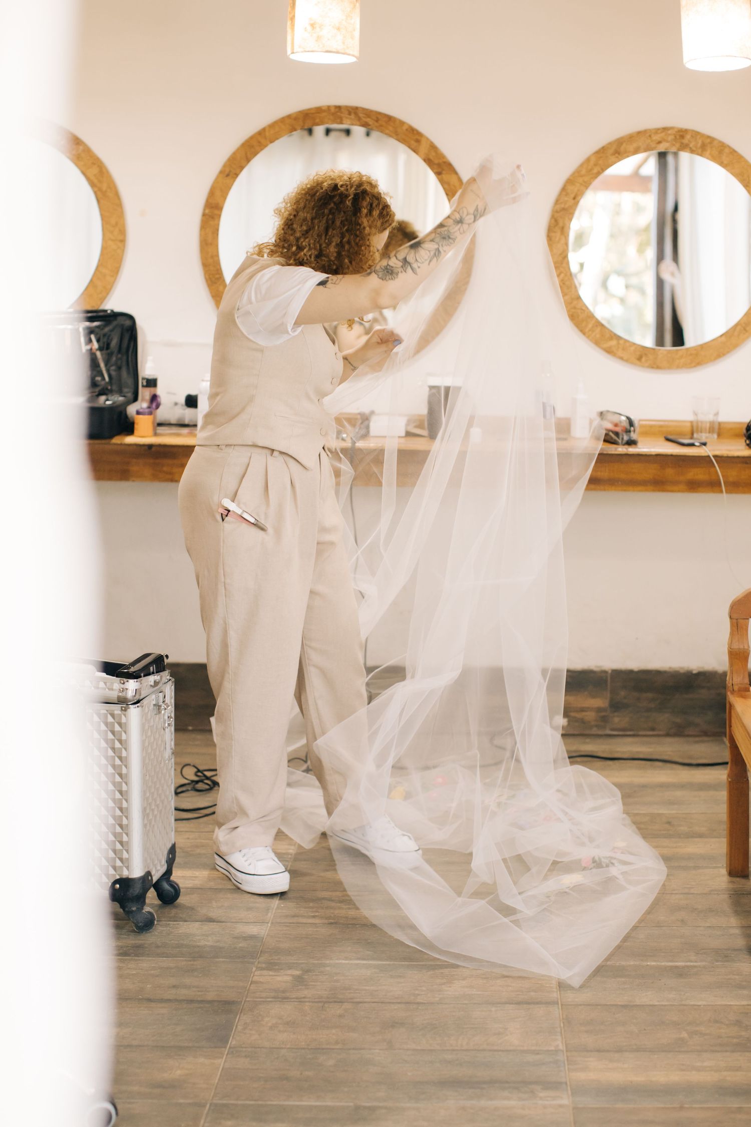 Hair stylist in beige outfit working with wedding veil in modern salon setting.