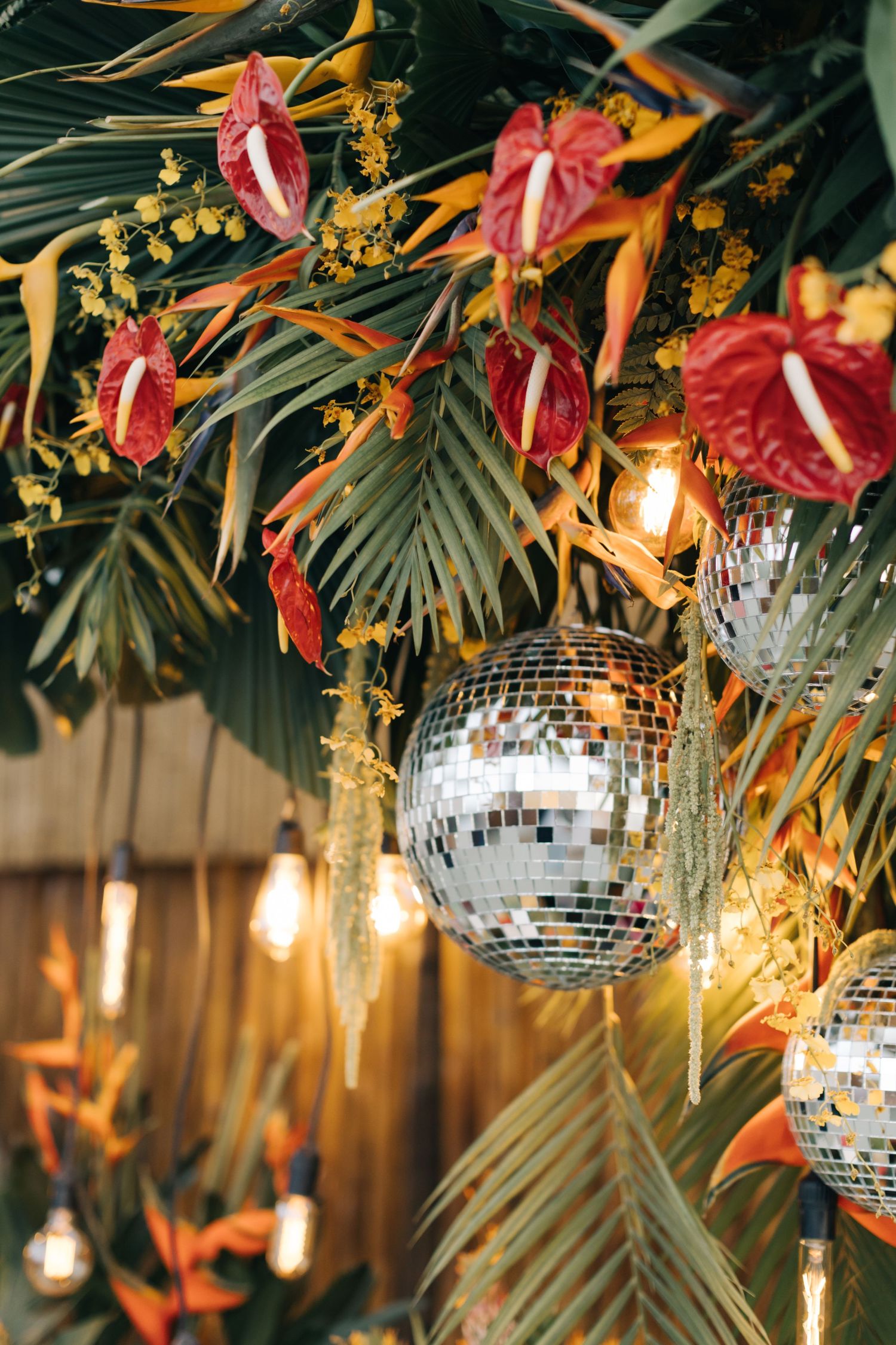 Disco balls and tropical flowers create festive overhead party decor with ambient lighting.