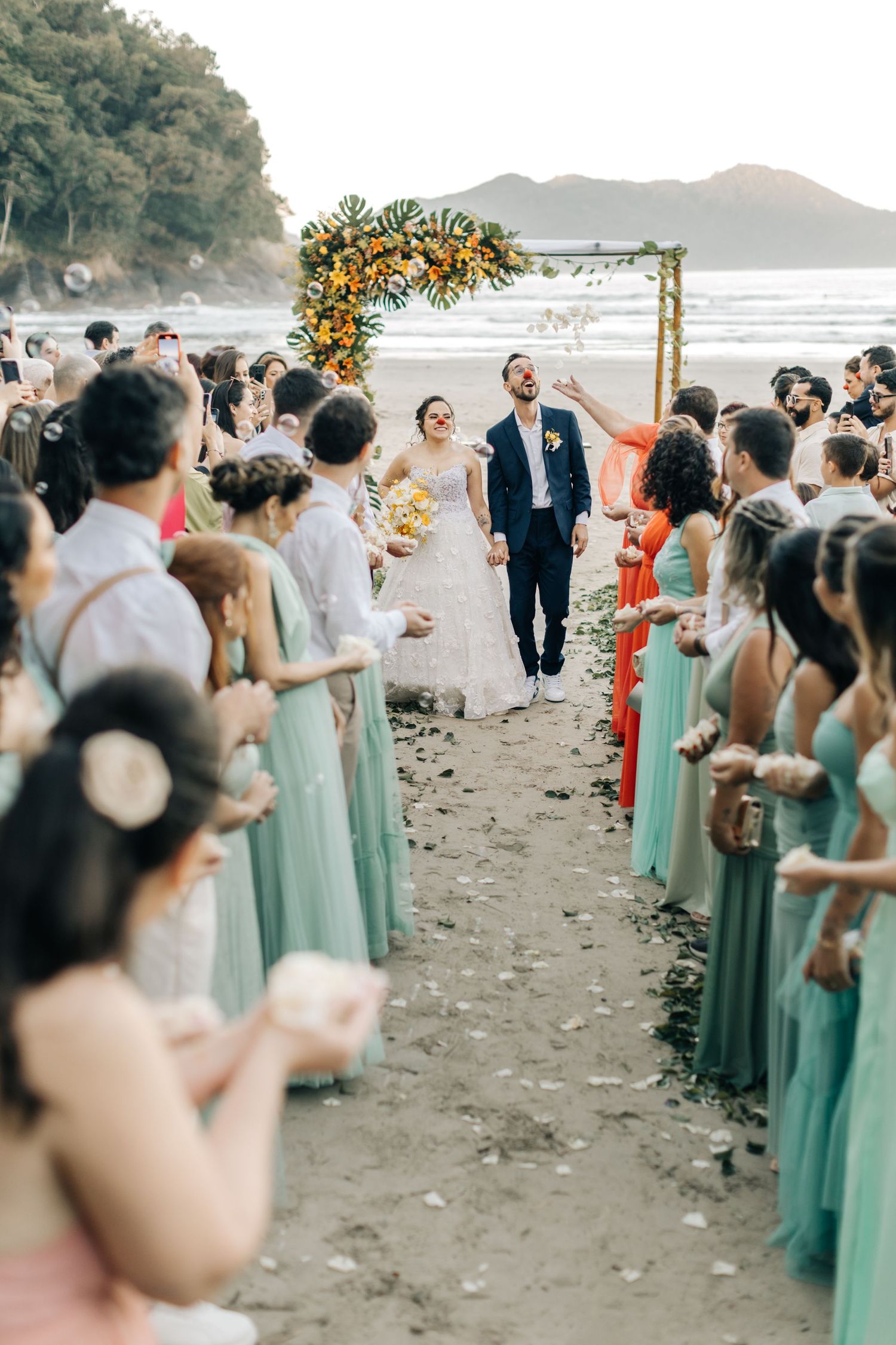 Wedding party in mint green dresses lines up on a beach during sunset ceremony.