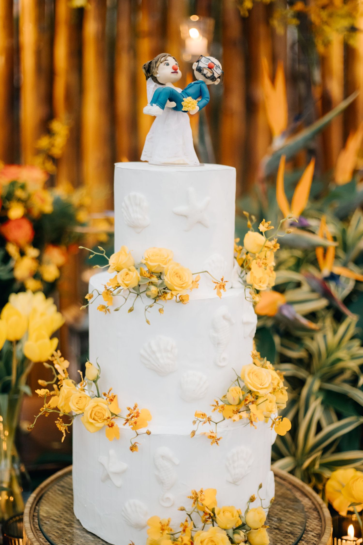 Elegant three-tier white wedding cake decorated with yellow flowers and a custom cake topper.