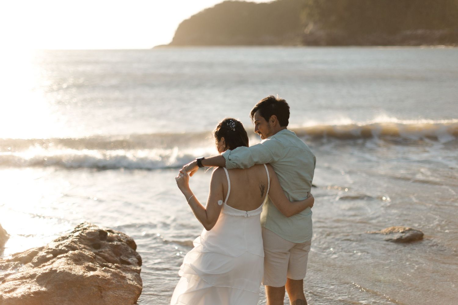Couple walking along a scenic beach shoreline during golden hour sunset.
