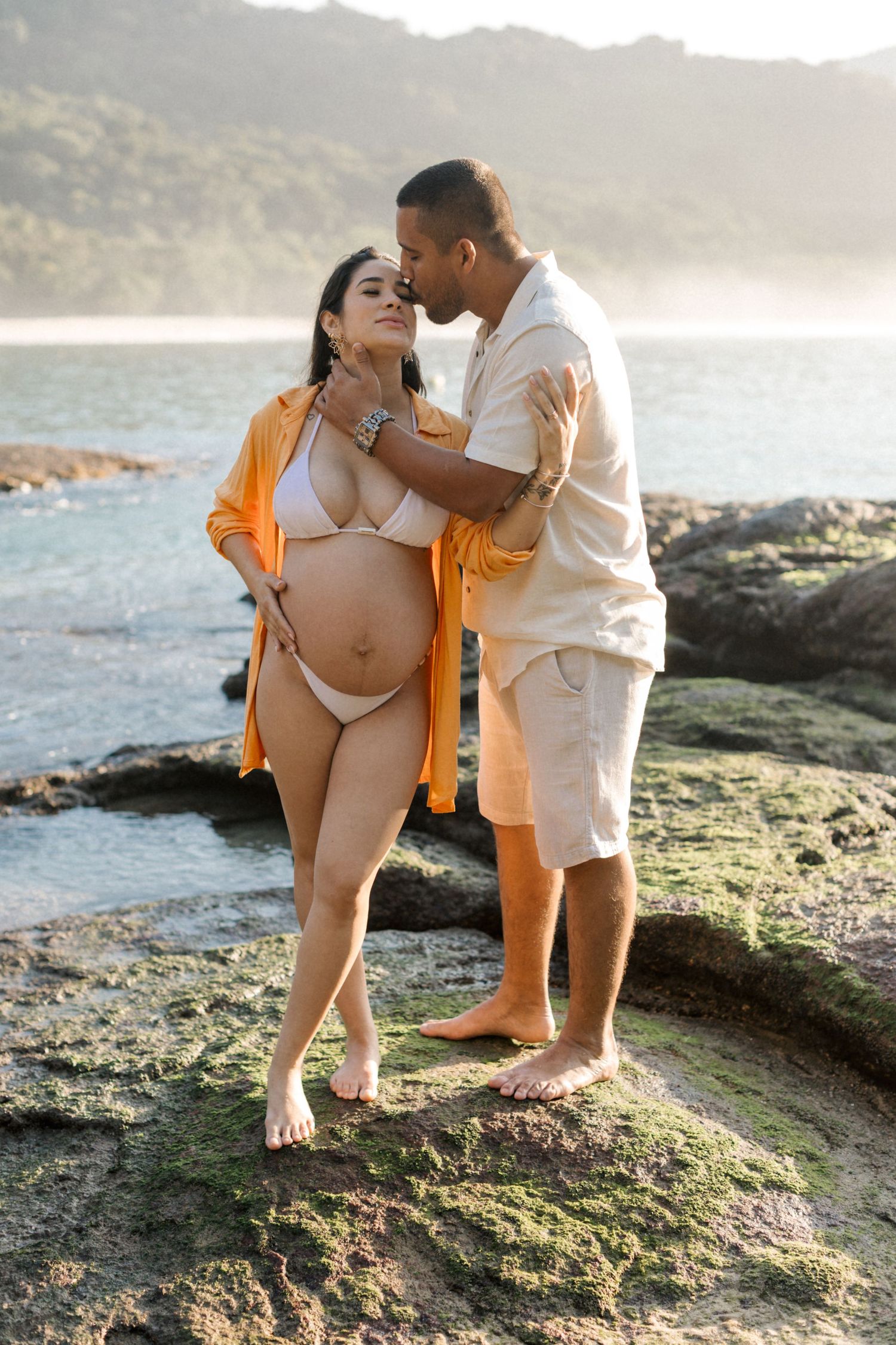 Maternity photoshoot on rocky beach during golden hour sunset.