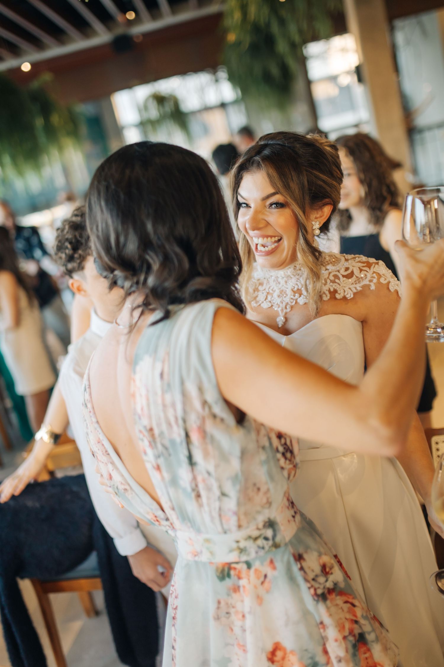 Wedding celebration candid moments showing guests in floral dresses hugging and laughing.