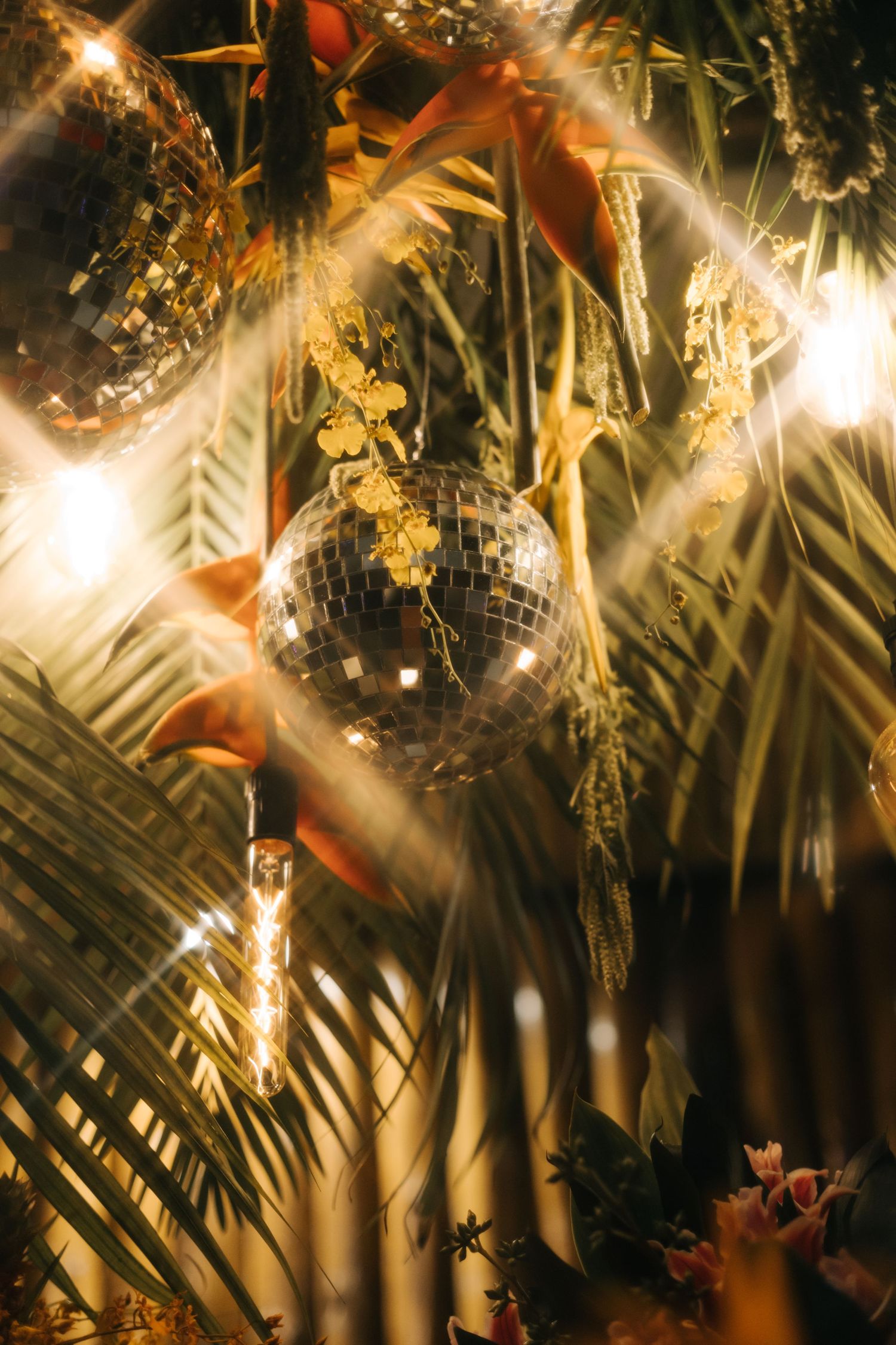 A disco ball reflects light through tropical palm leaves creating a magical party atmosphere.