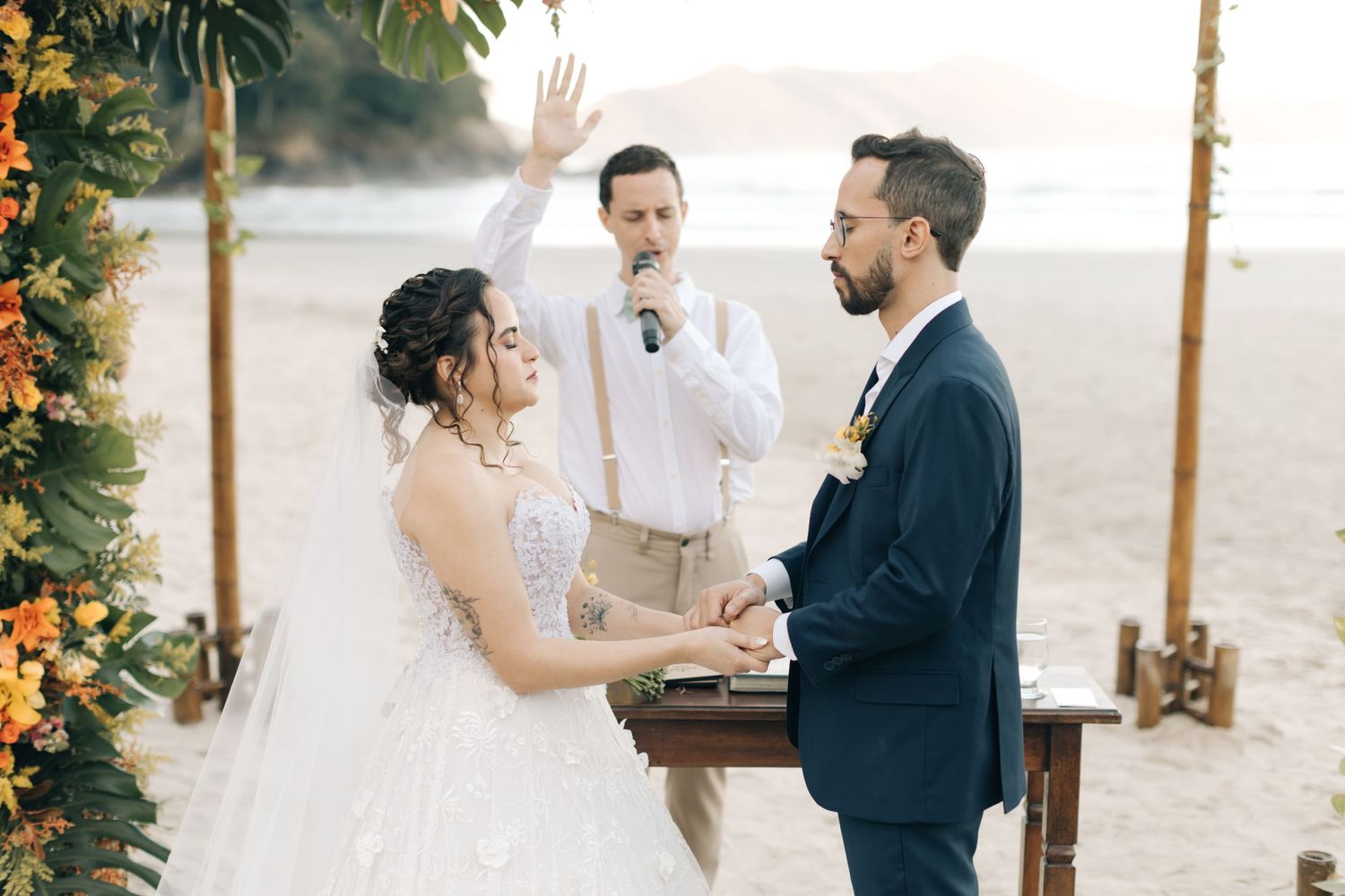 Couple exchanges vows under floral arch during beach wedding ceremony.