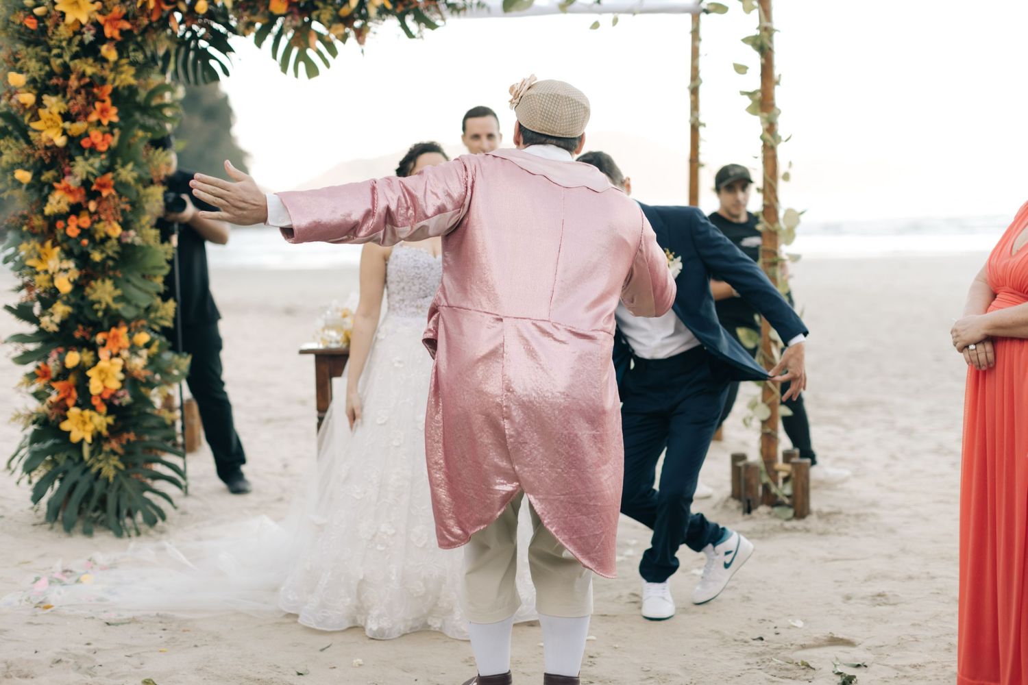 Figure in pink outfit gestures dramatically during outdoor wedding celebration.