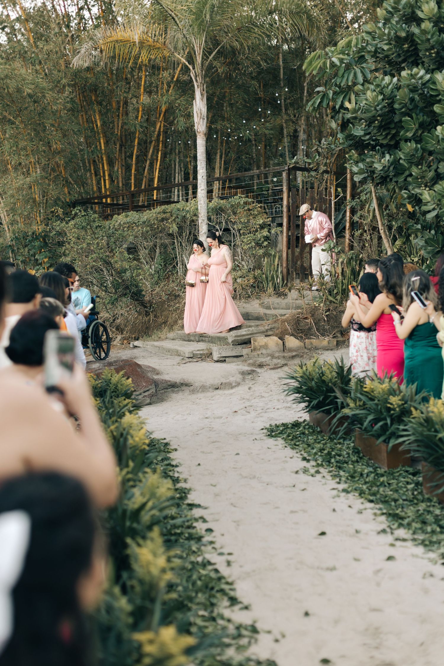 Wedding photographers capture bridesmaids in pink dresses walking down a garden path.
