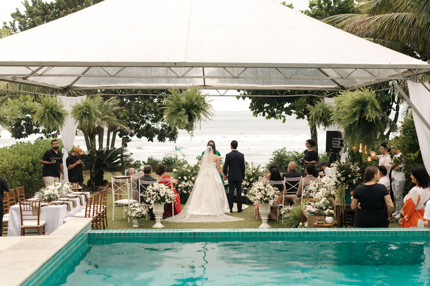 Outdoor wedding ceremony setup next to a swimming pool with white tent and floral decorations.