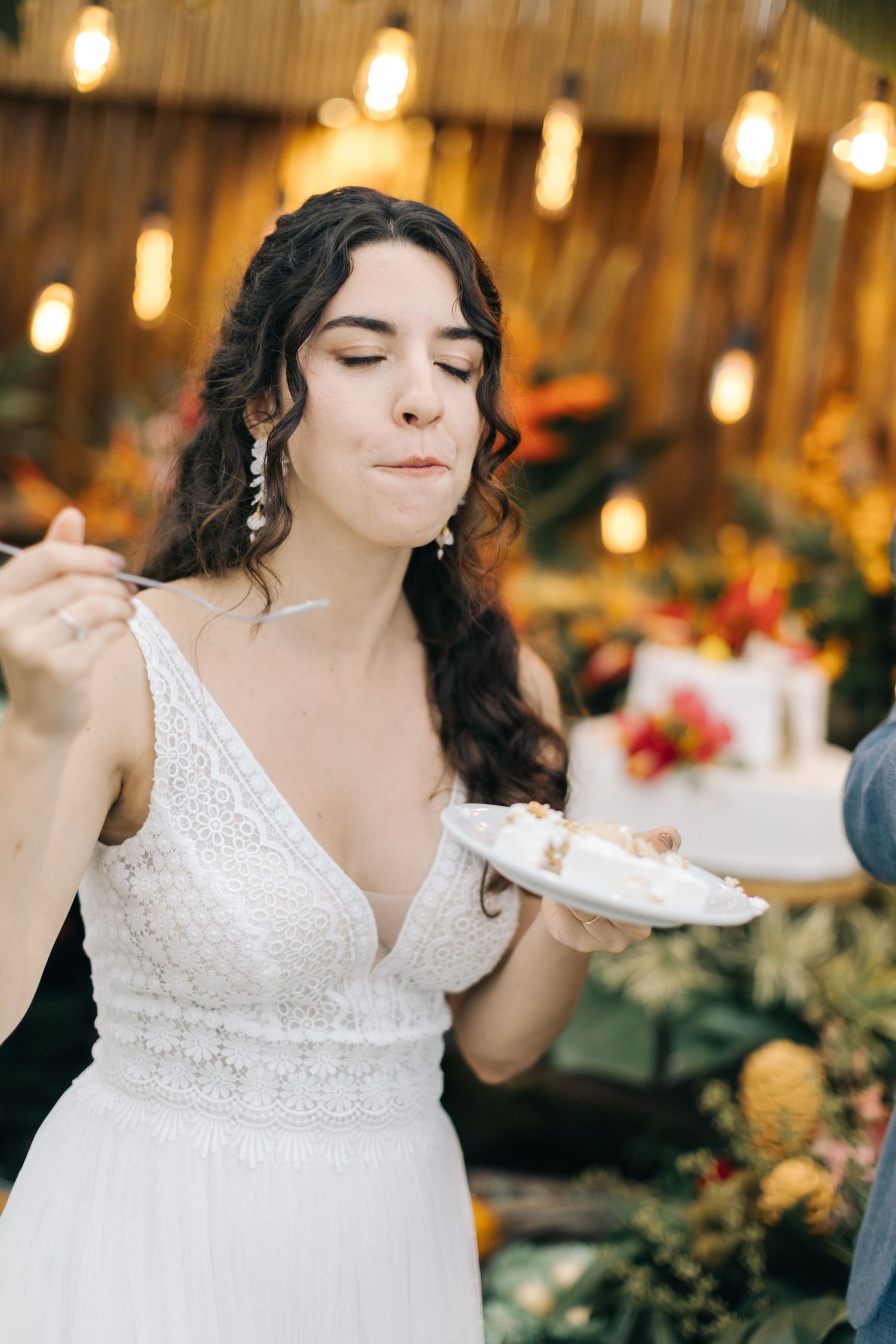 Bride in lace white dress savoring wedding cake at tropical-themed reception.