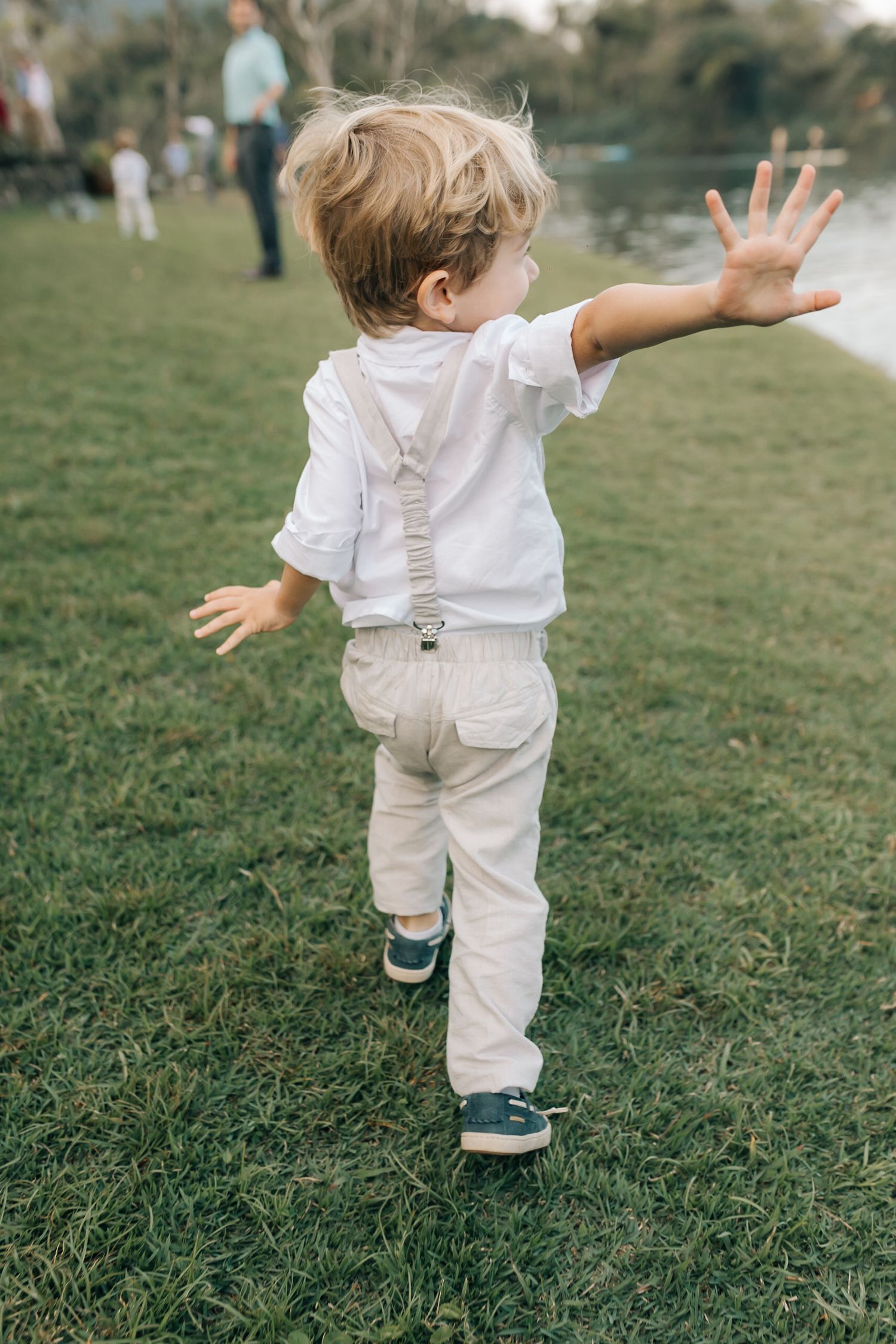 A young child in white clothing runs with arms outstretched on a grassy lawn.