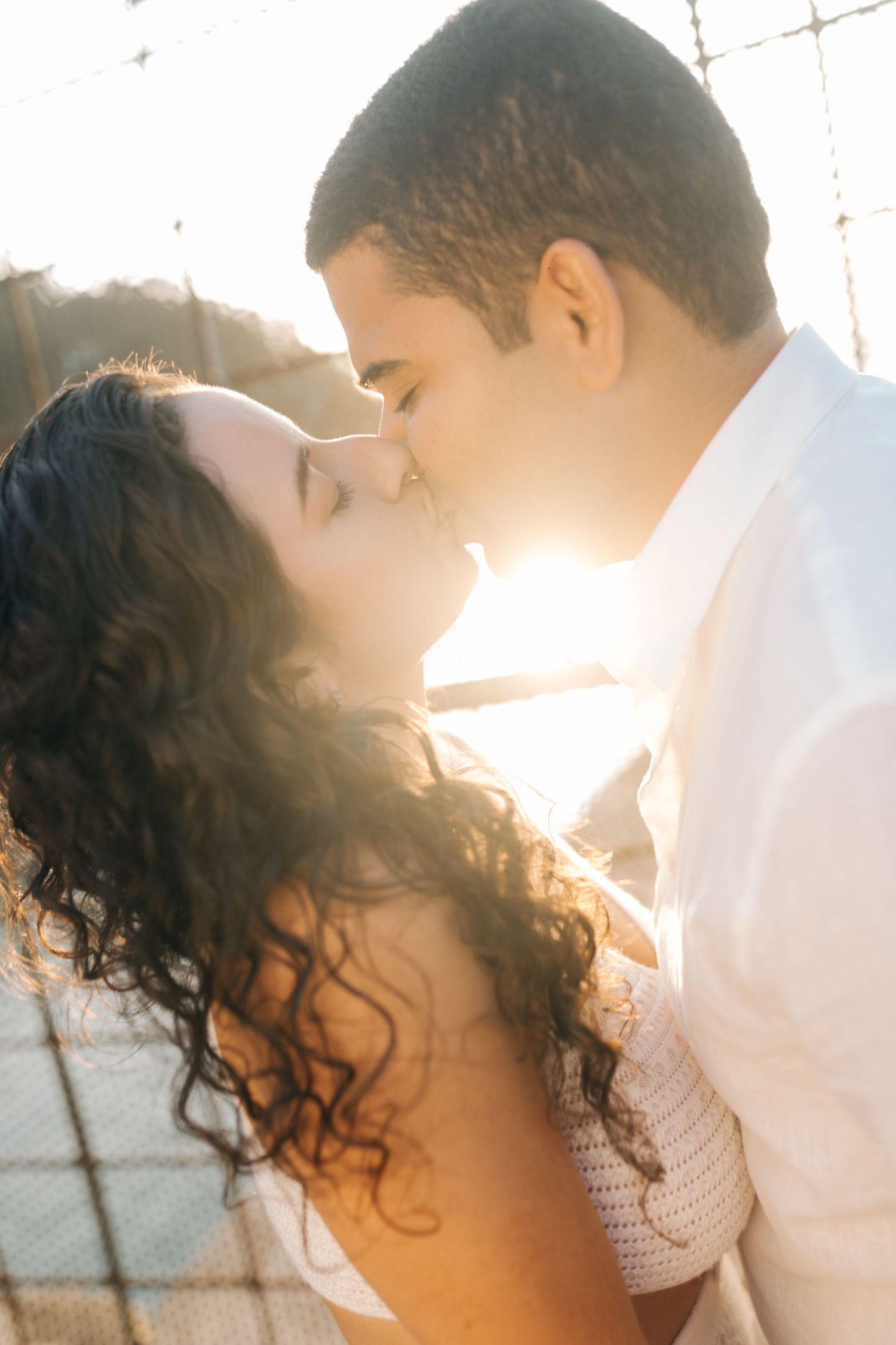 Backlit romantic portrait of couple sharing tender kiss against bright sunlight.