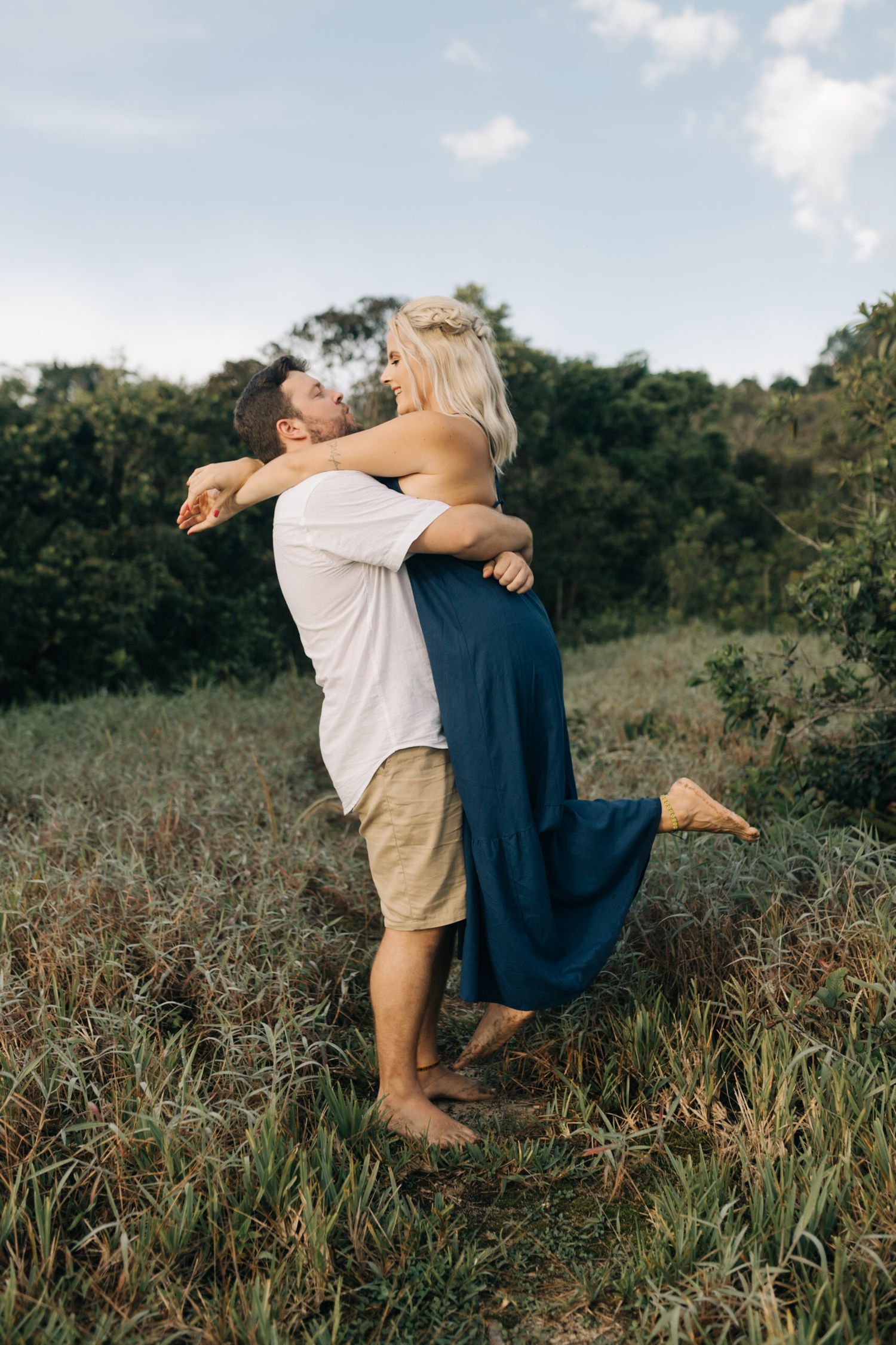 Playful lift pose captured against a backdrop of coastal hills and blue sky.