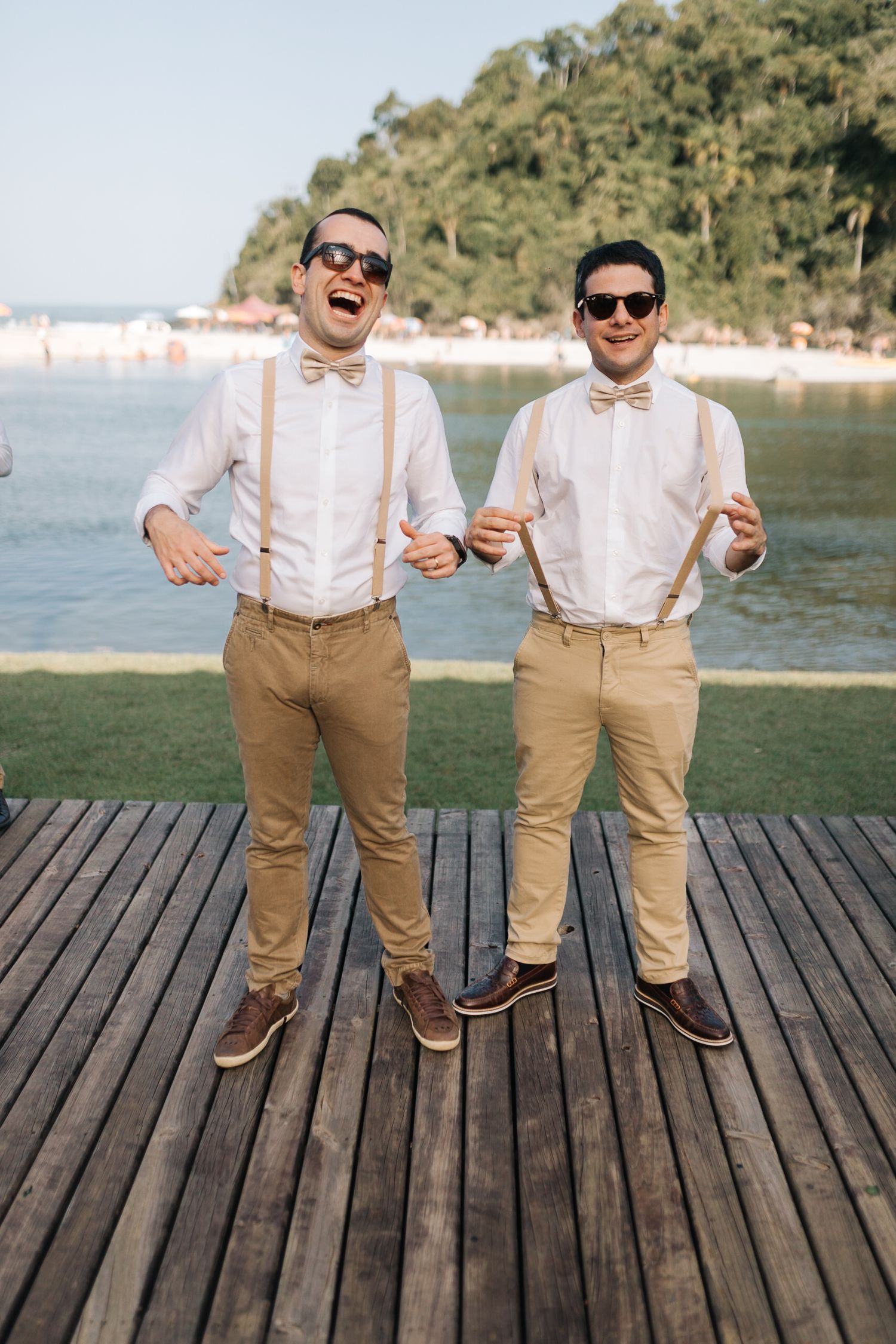 Groomsmen in suspenders and khaki pants pose playfully on wooden dock.