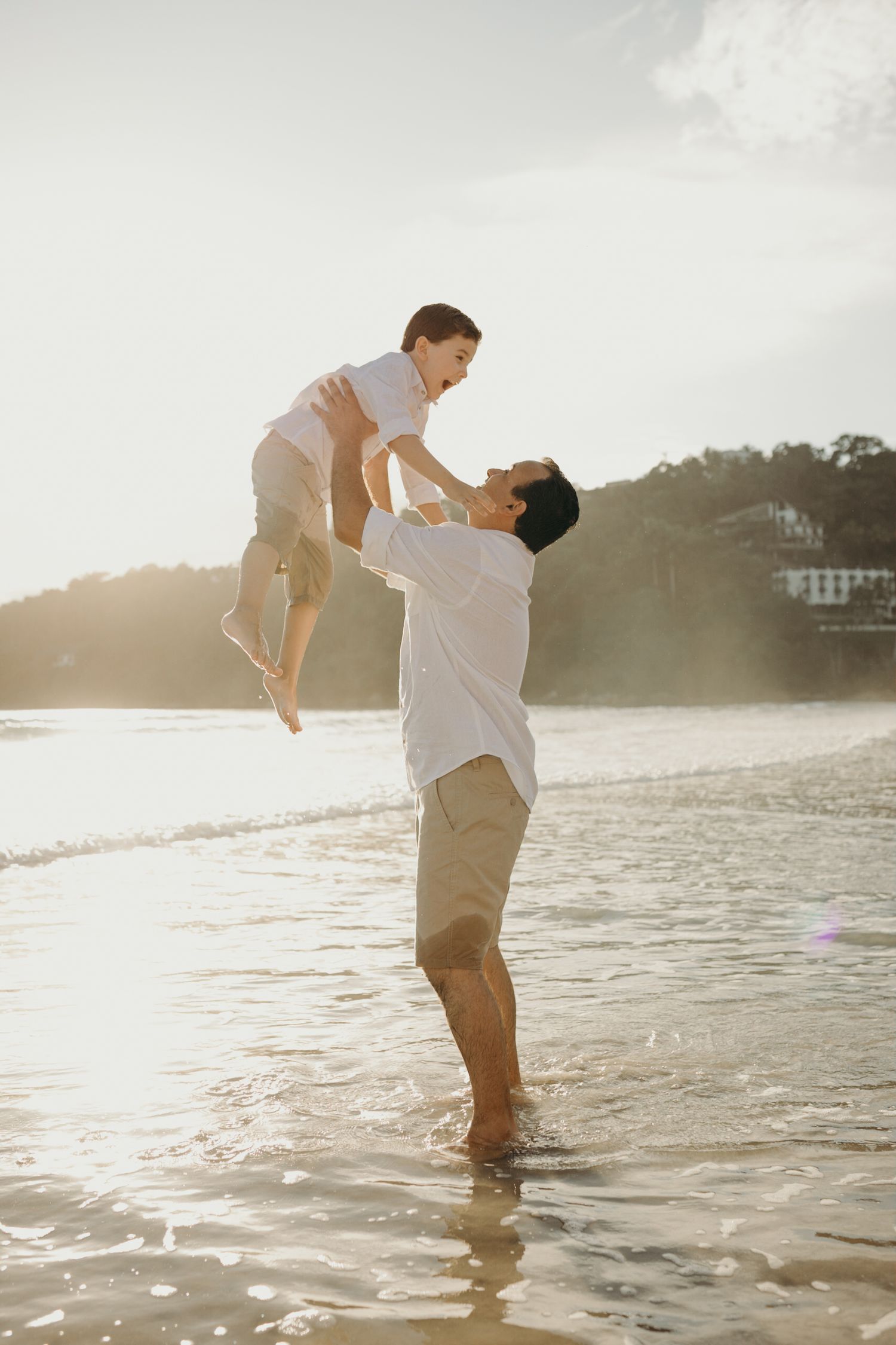 A joyful lifting moment between two people playing on a sunlit beach.