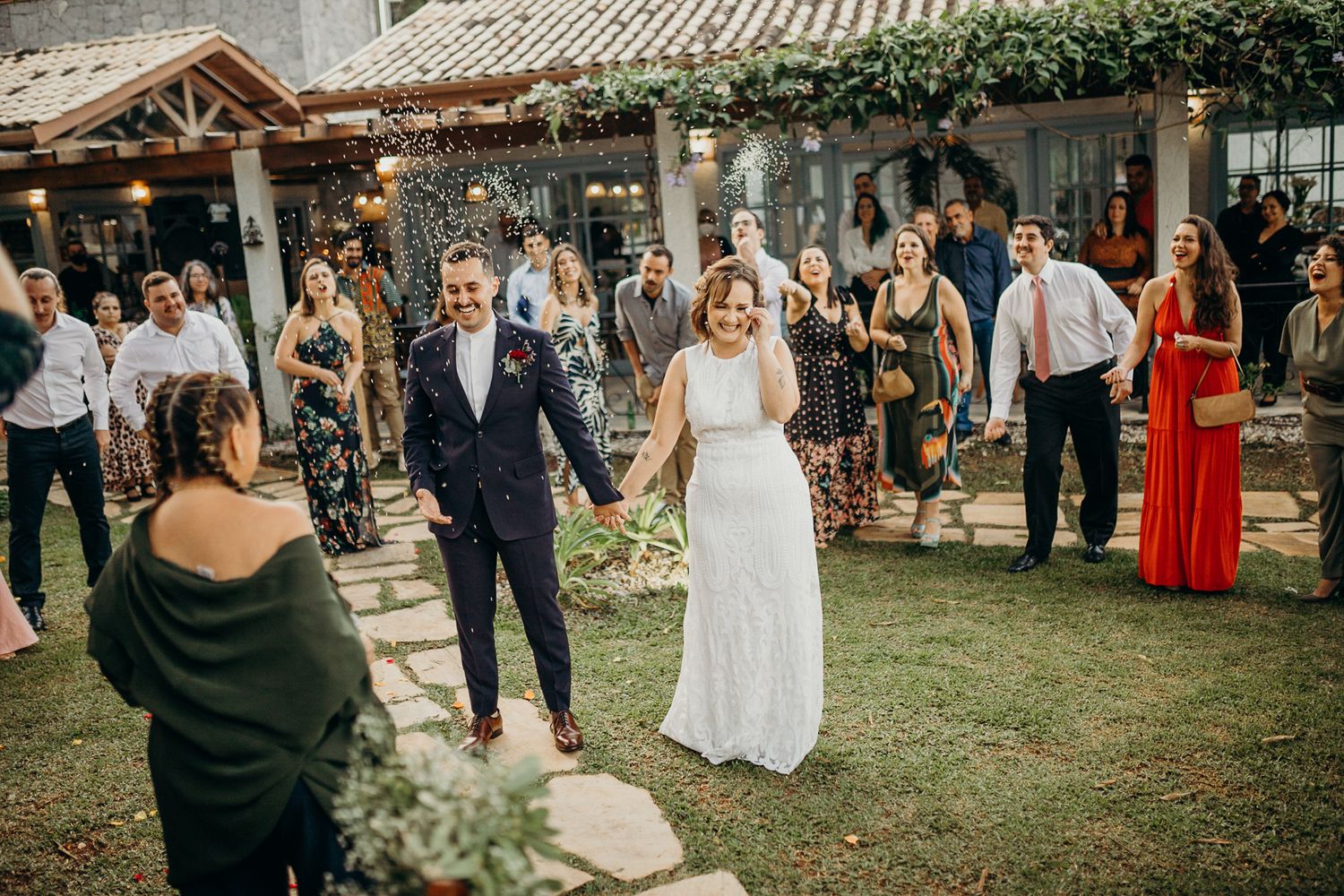 An outdoor wedding ceremony setup with guests gathered on grass near a Spanish-style building.