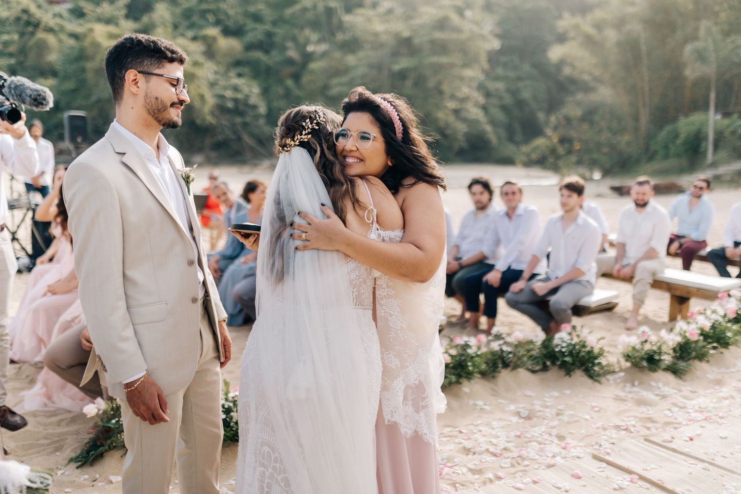 A touching moment during a beach wedding ceremony with guests seated on the sand.