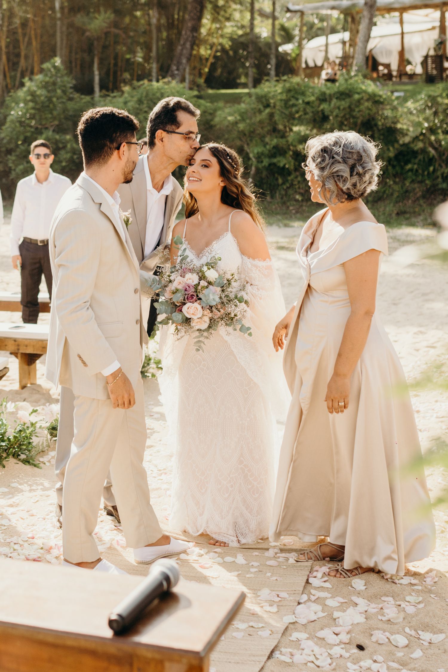 Wedding party in white and cream colored attire gather during outdoor beach ceremony.