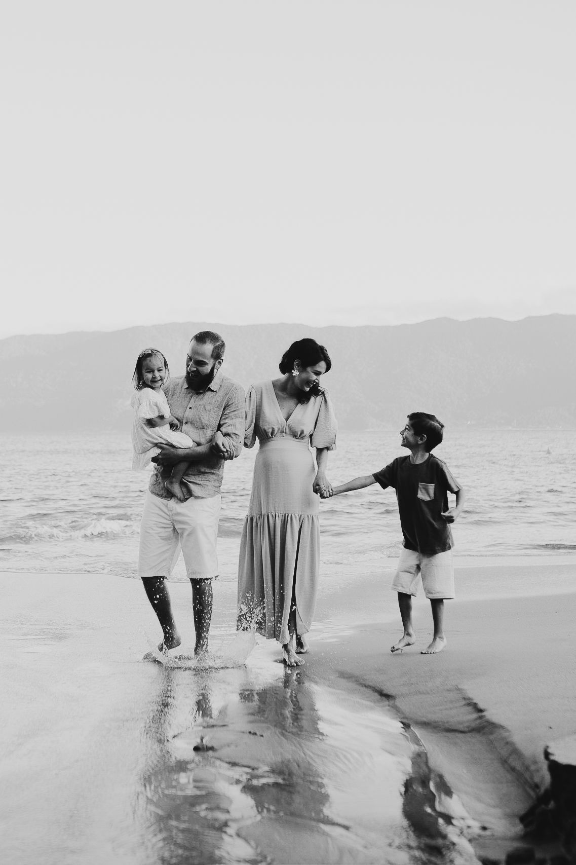 People walk together along the beach shoreline in black and white photography.