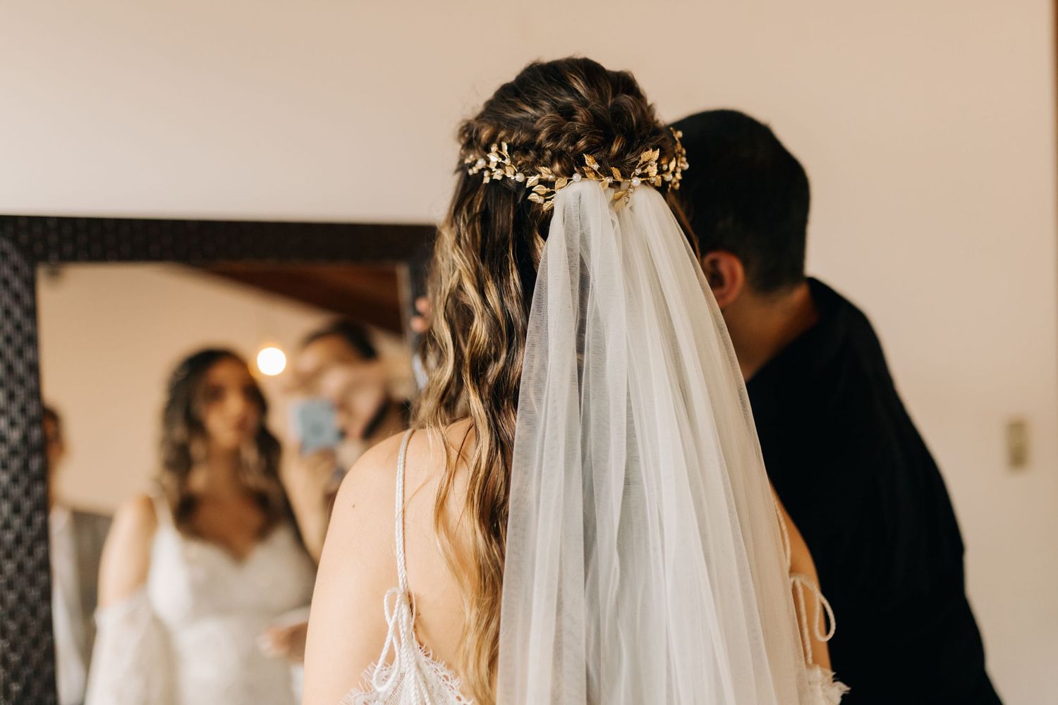 Back view of a bride with an ornate golden headpiece and flowing veil during wedding preparations.