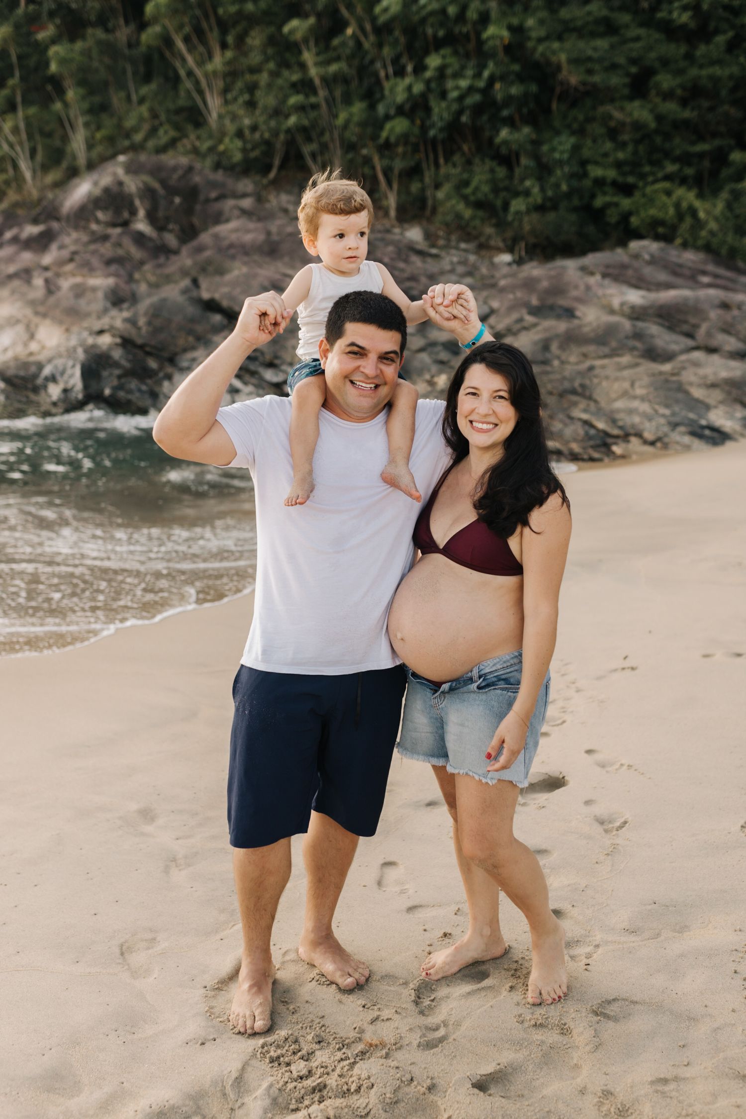 Family having fun and posing playfully on a sandy beach with rocky backdrop.