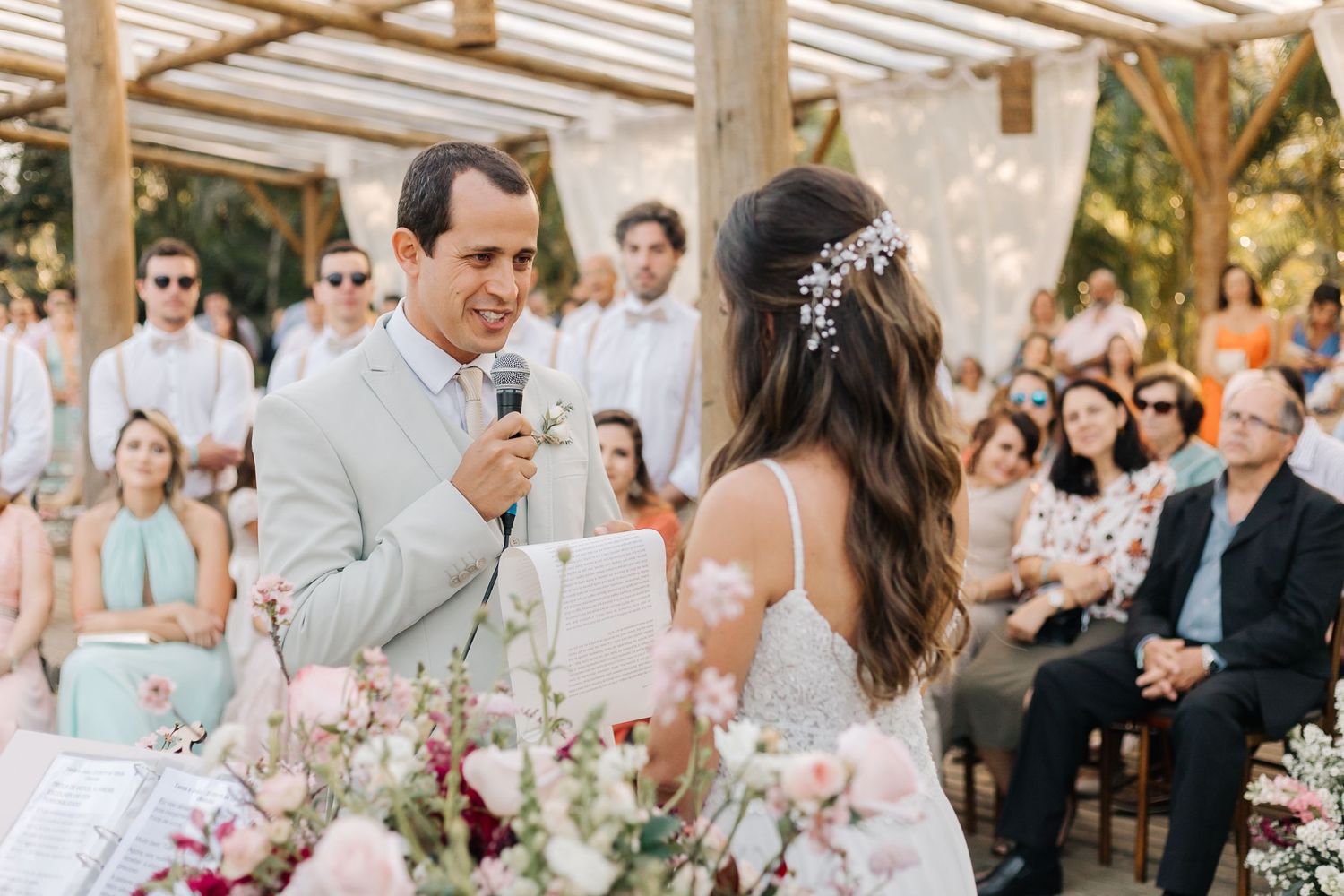 Wedding ceremony with guests watching under wooden pergola adorned with flowers.