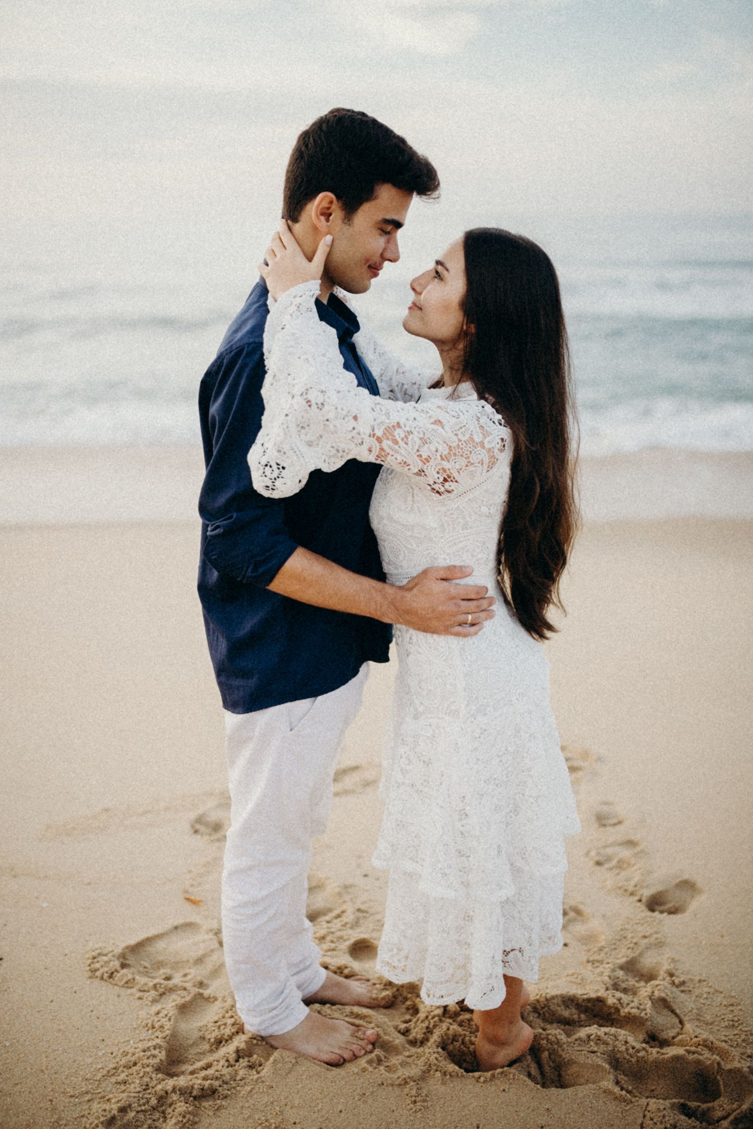 Intimate beach portrait of a couple in coordinated navy and white outfits embracing on the sand.