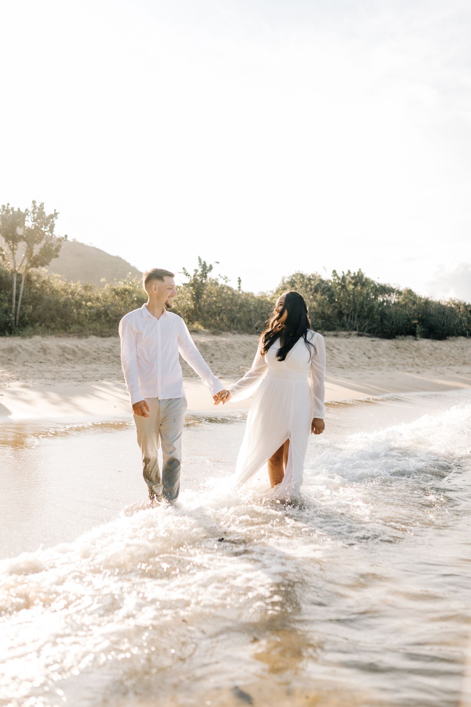 A couple enjoys splashing in ocean waves during a beach photoshoot.
