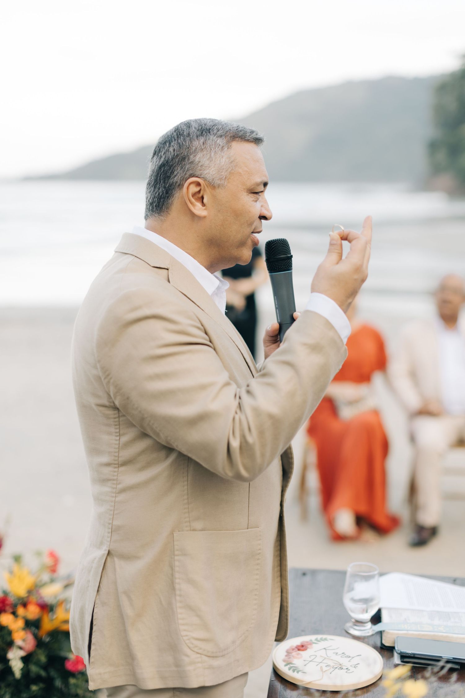 Person in a beige suit jacket gestures emotionally while speaking at a beachside event.