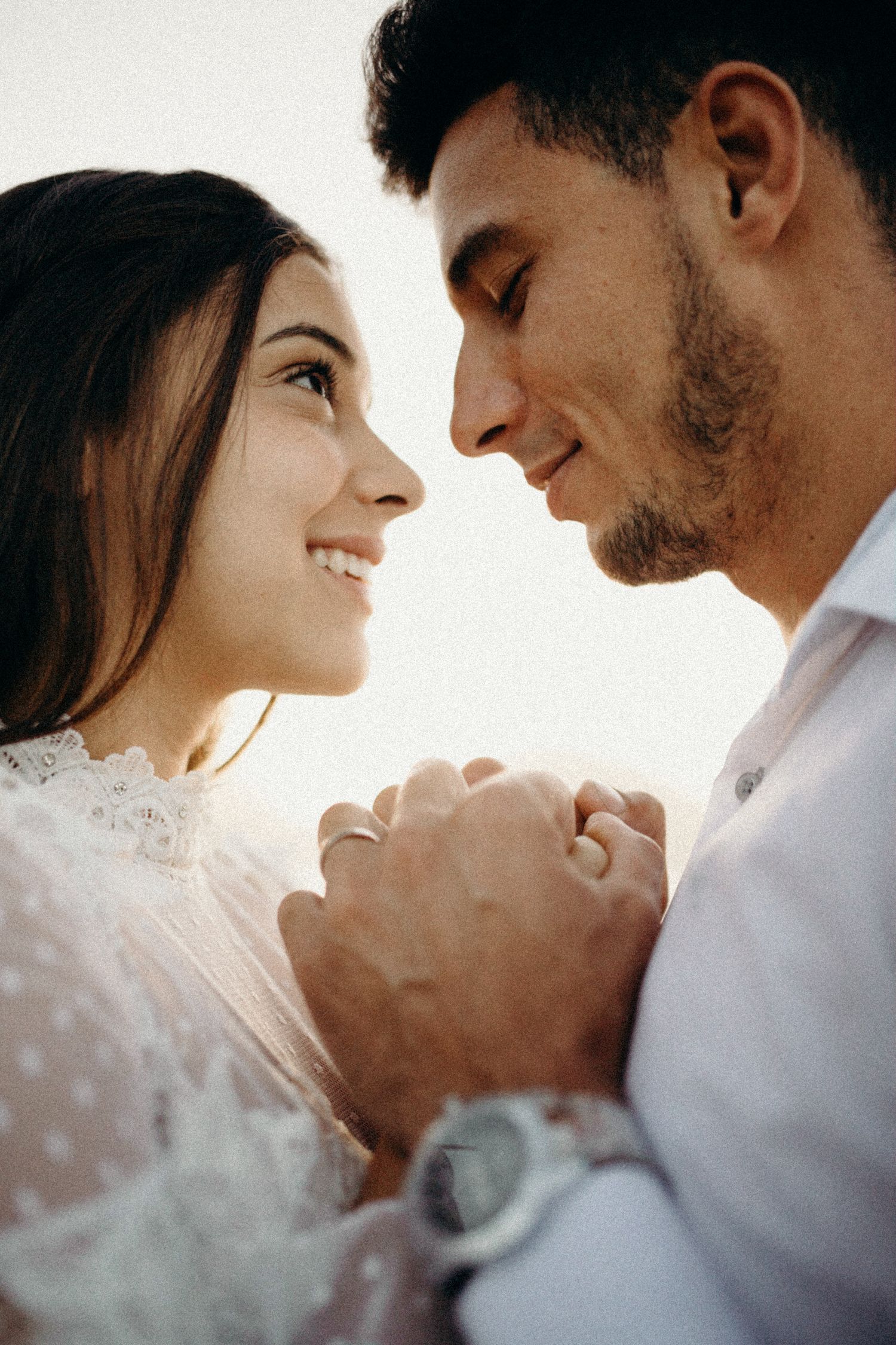 A romantic couple holds hands and gazes lovingly at each other in an intimate close-up moment.