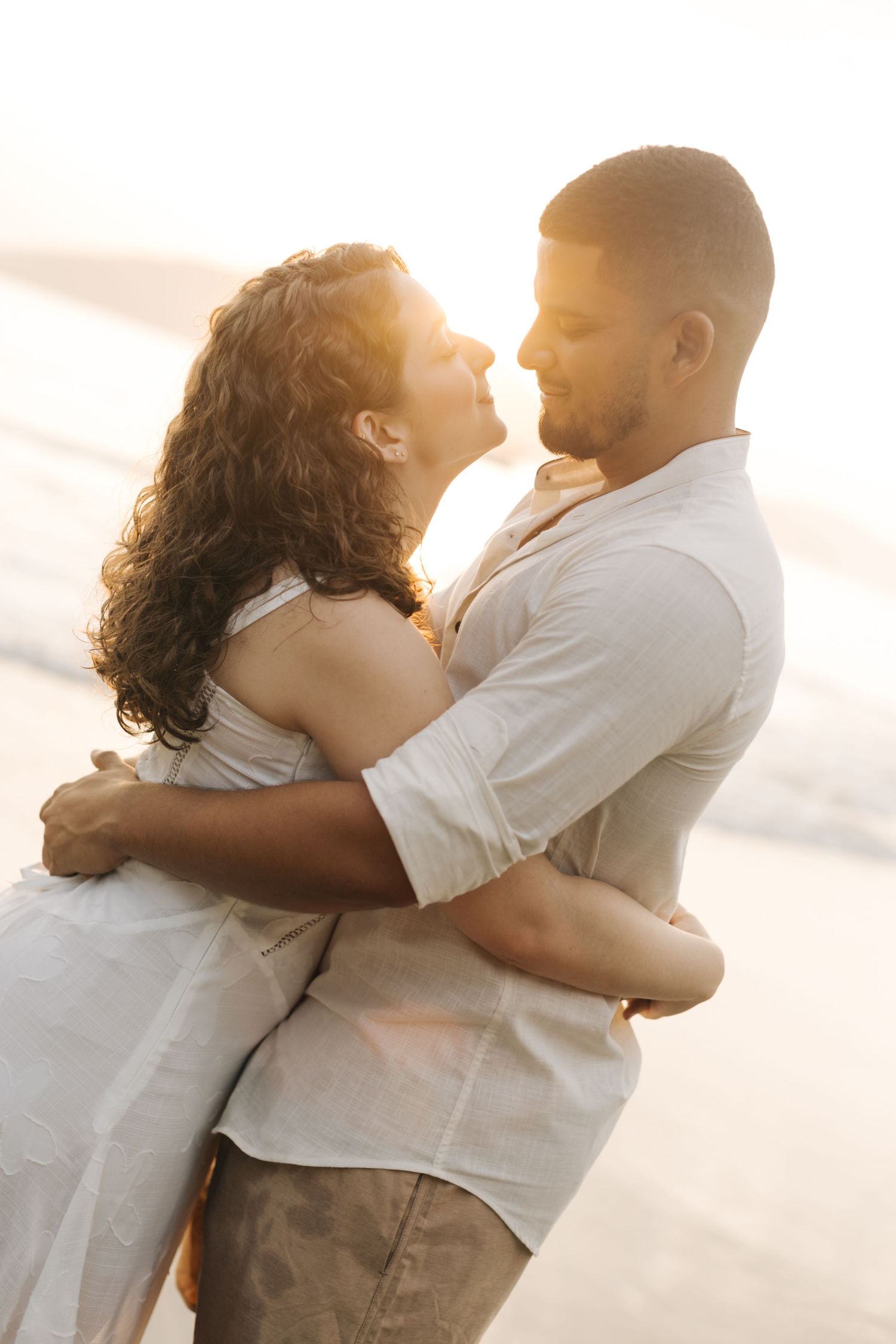 A tender moment between a couple in white clothing on a sunset beach.