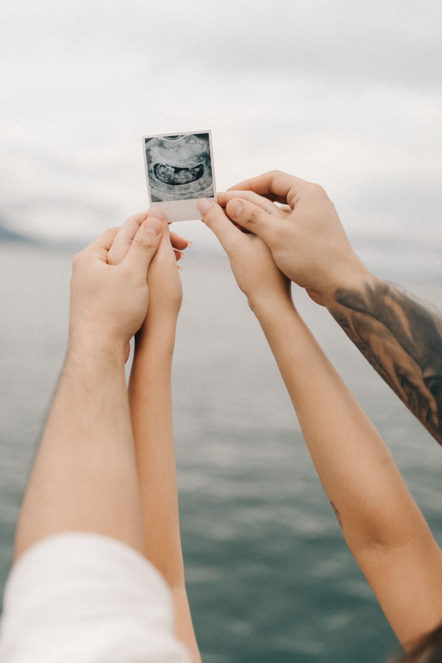 Hands holding up a small photograph against an ocean backdrop.