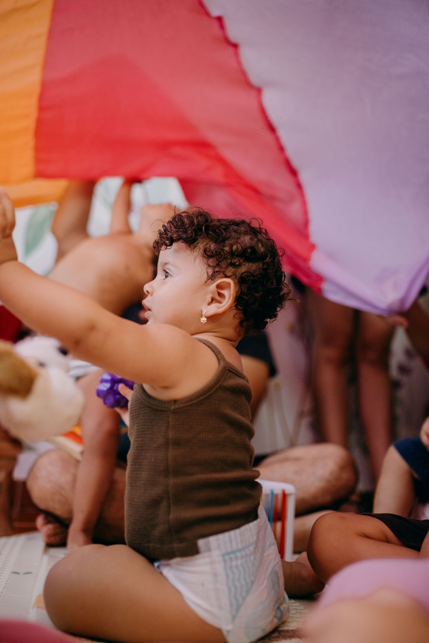 Small child in brown outfit reaching up toward colorful fabric canopy.