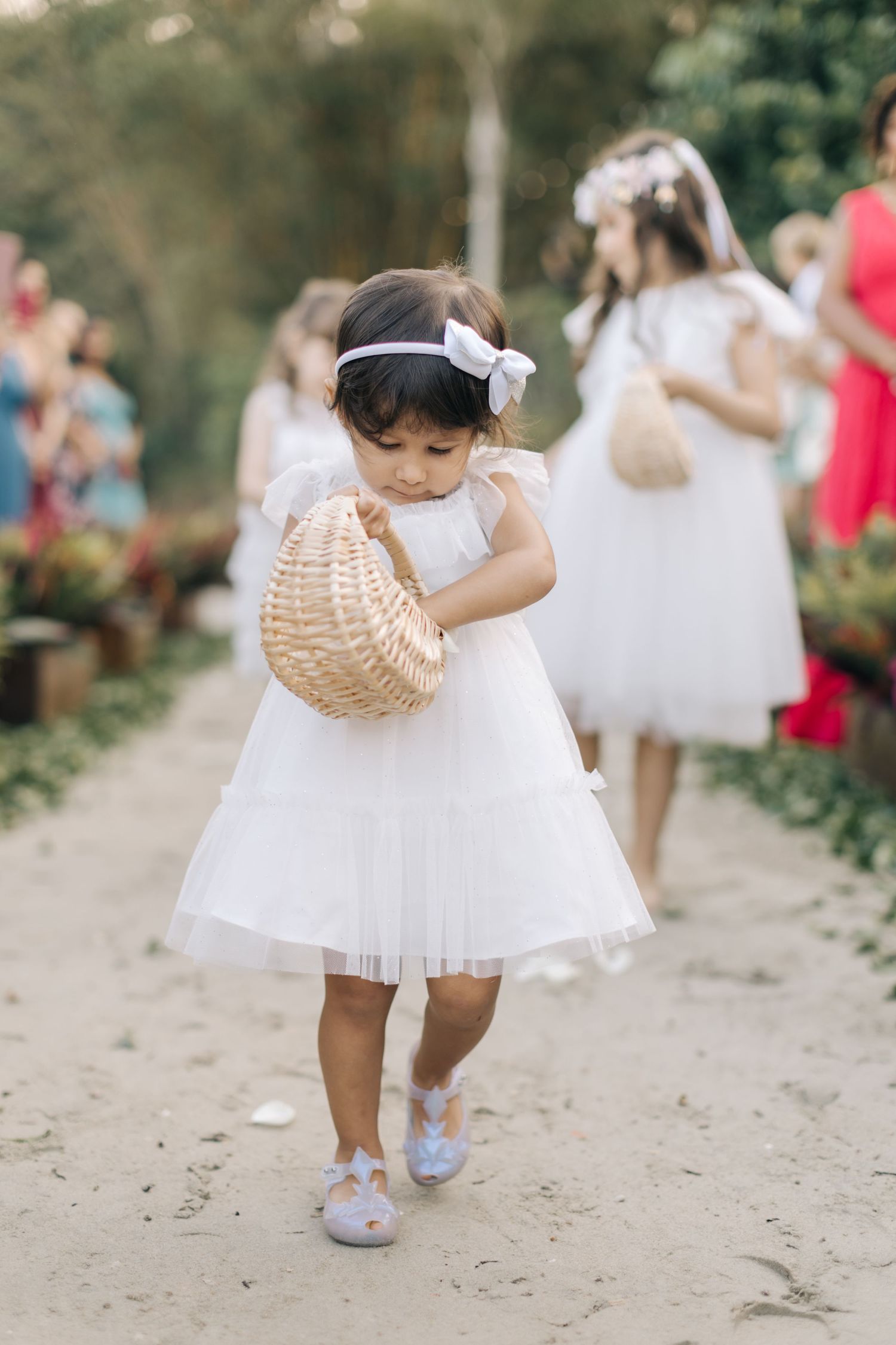 Little girl in white dress twirling with a wicker basket on a garden path.