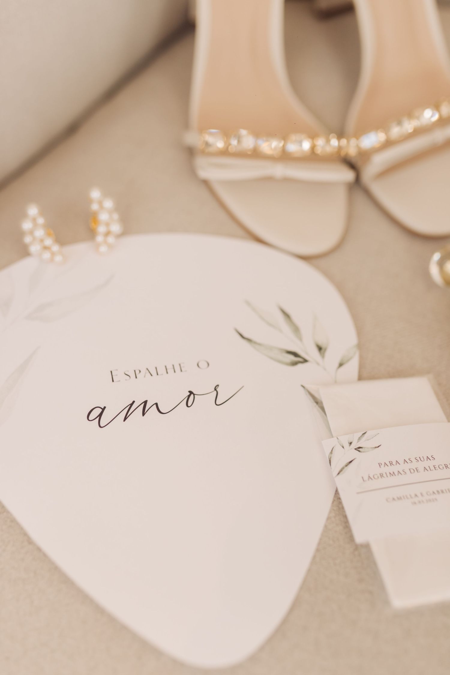 Wedding stationery with 'amor' text and delicate floral design next to pearl-adorned bridal shoes.