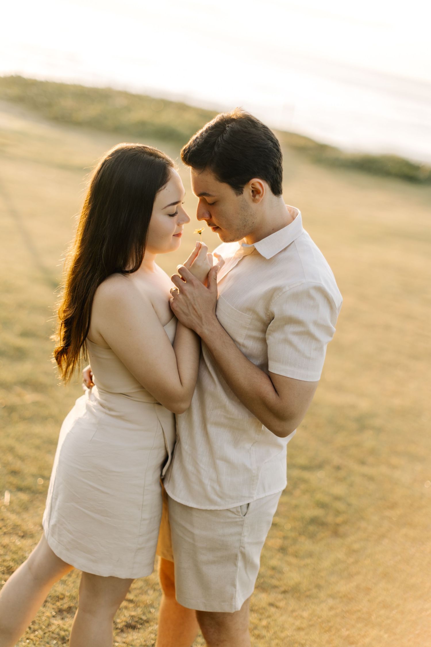 Intimate portrait of couple in light-colored attire sharing a close embrace in warm sunset light.