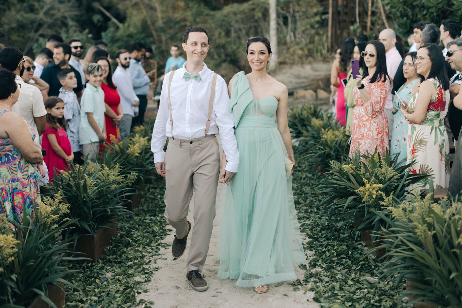 Wedding party members walk along a landscaped pathway lined with tropical plants.