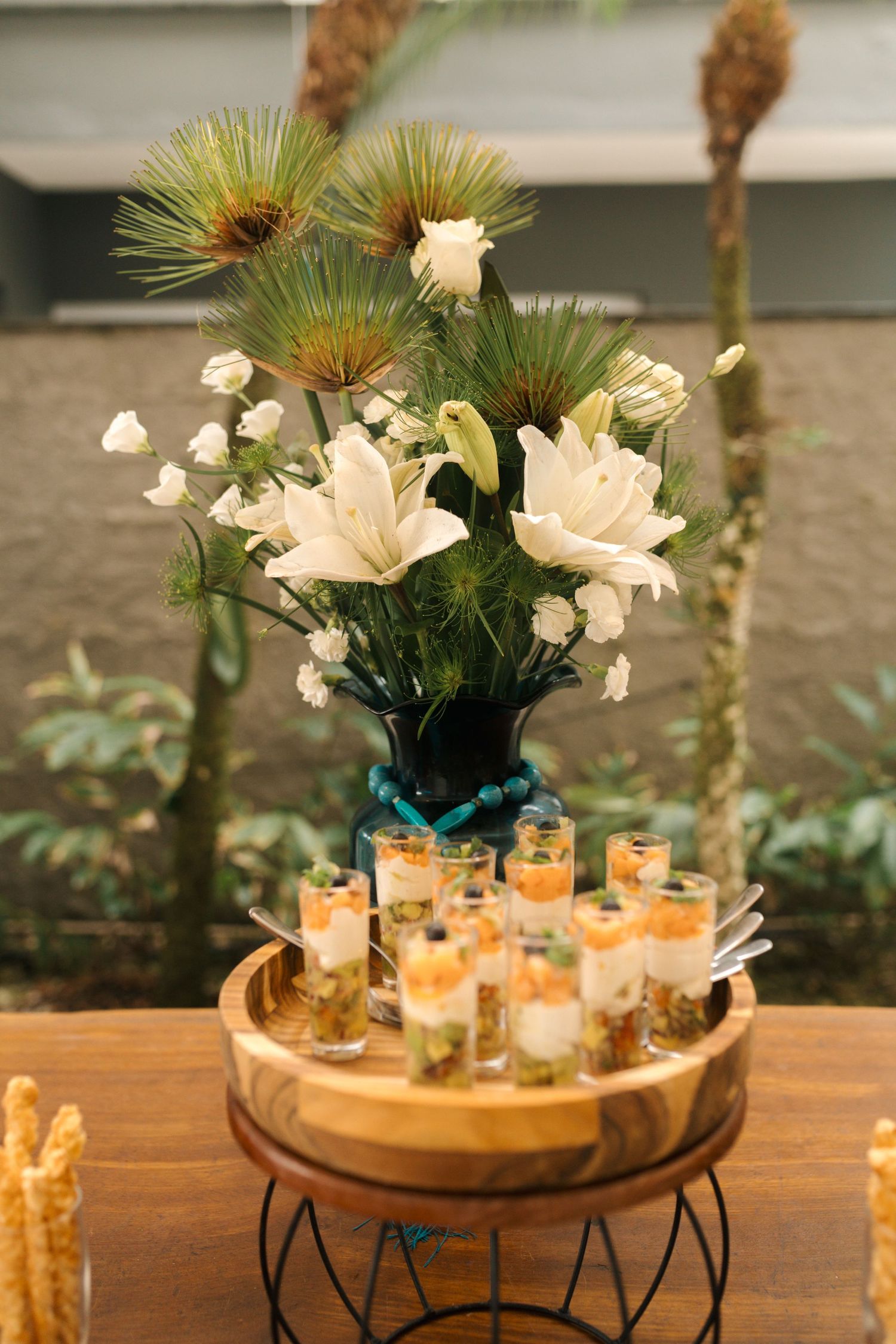 Floral arrangement with lilies and palm fronds above a tray of candlelit appetizers.