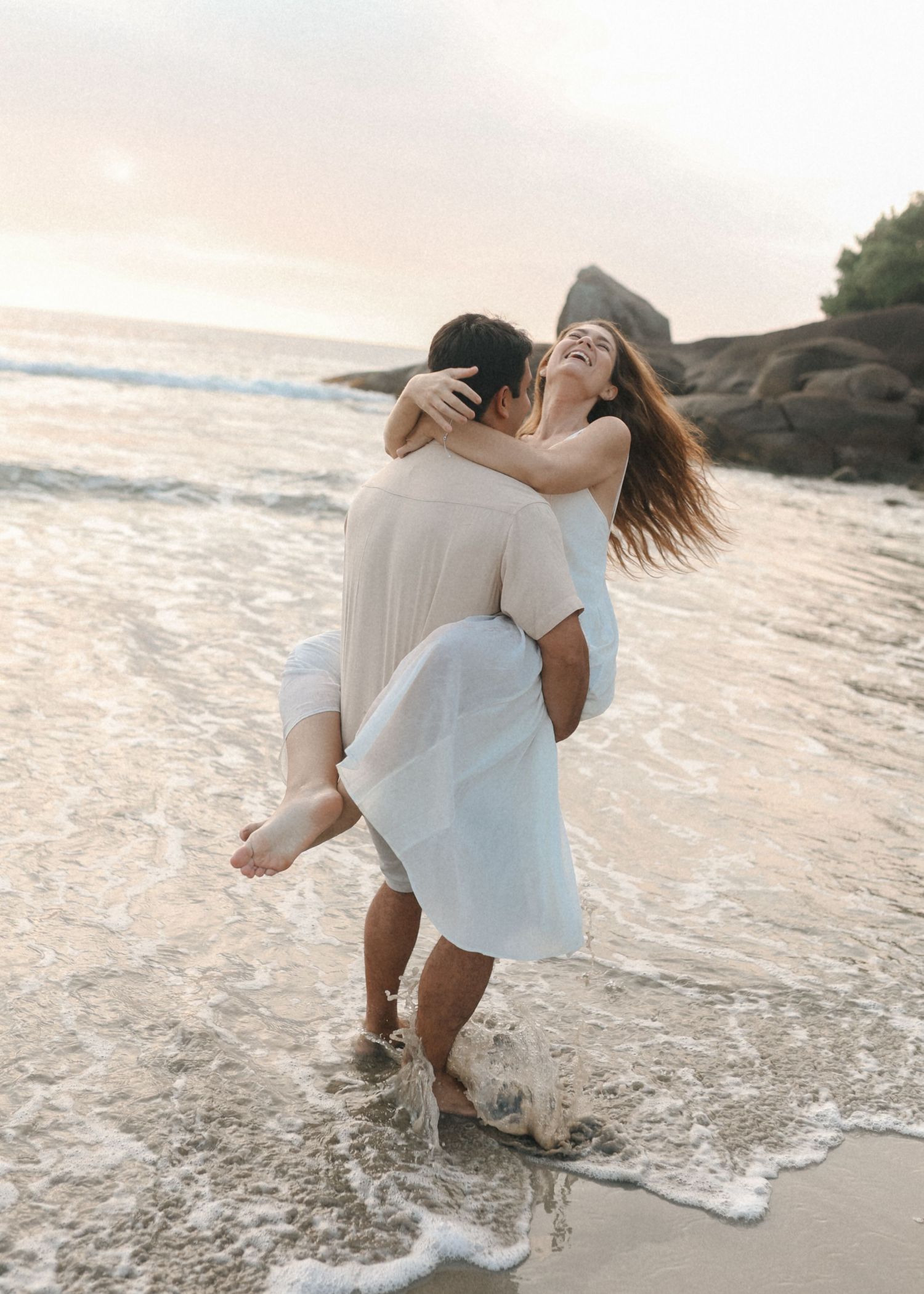 A playful moment captured as a couple spins together at the ocean's edge during sunset.