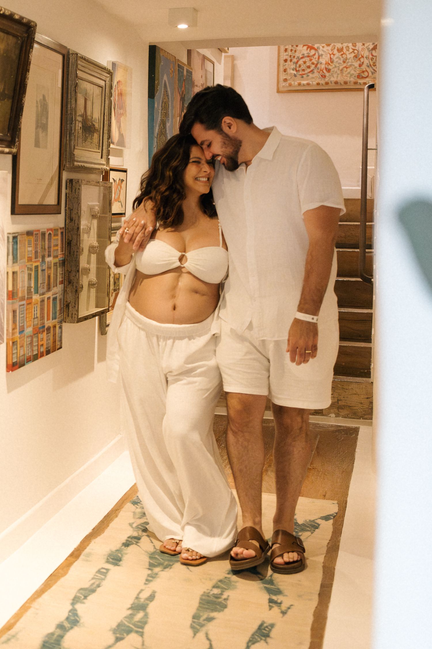 People in white clothing walking through a gallery hallway with artwork displayed on walls.