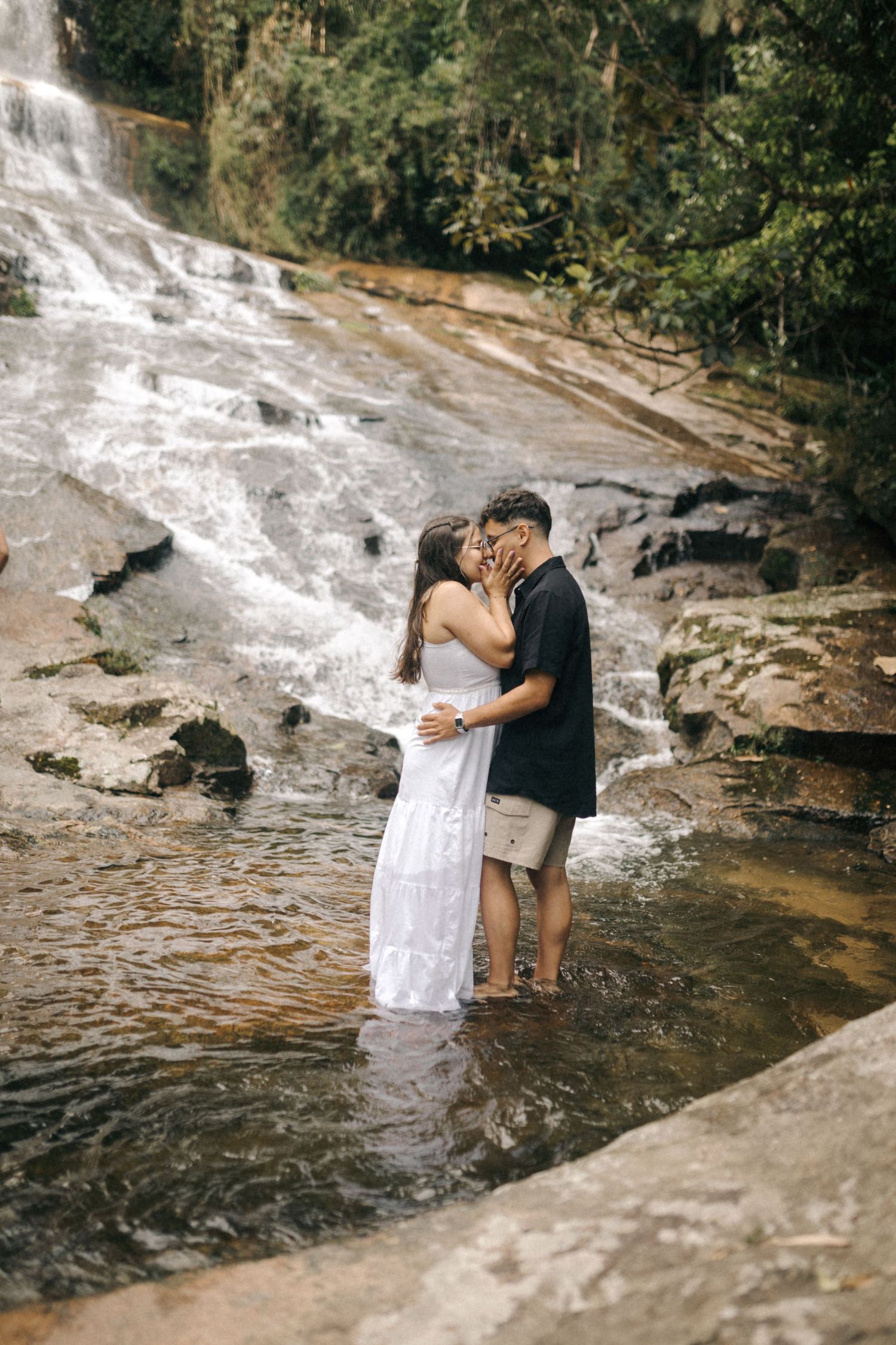 Romantic embrace in shallow water at the base of a cascading waterfall.