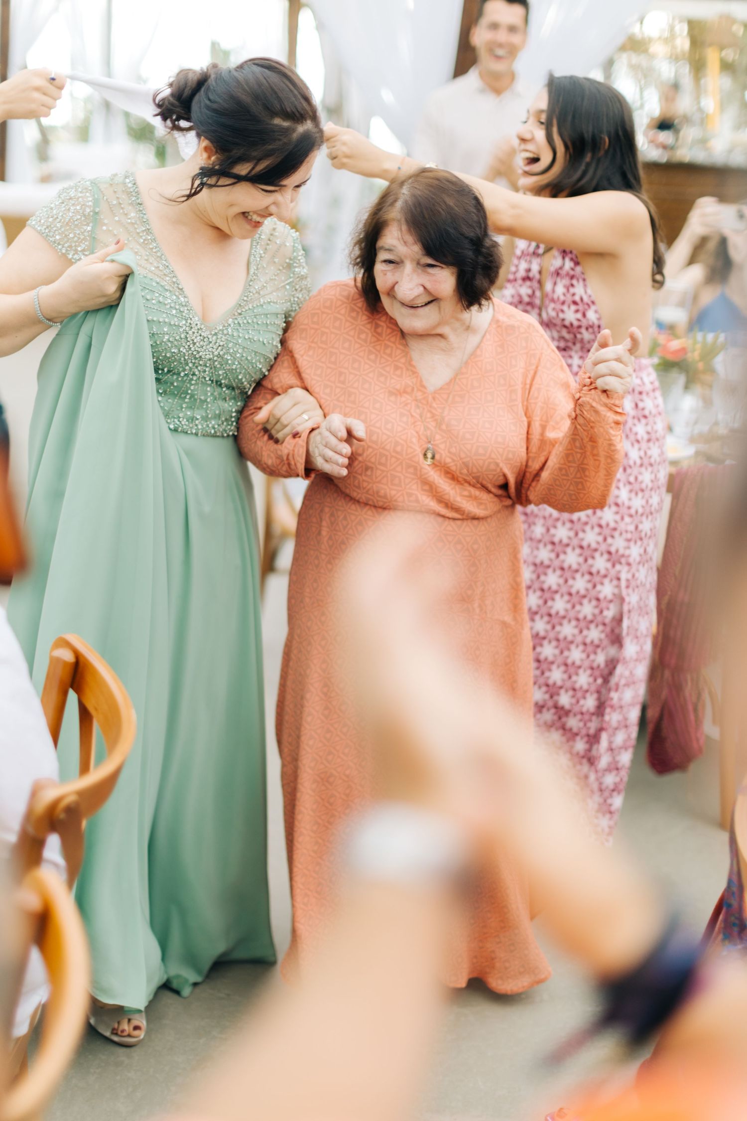 Attendees in formal attire dance together at a celebratory event wearing mint green and coral dresses.